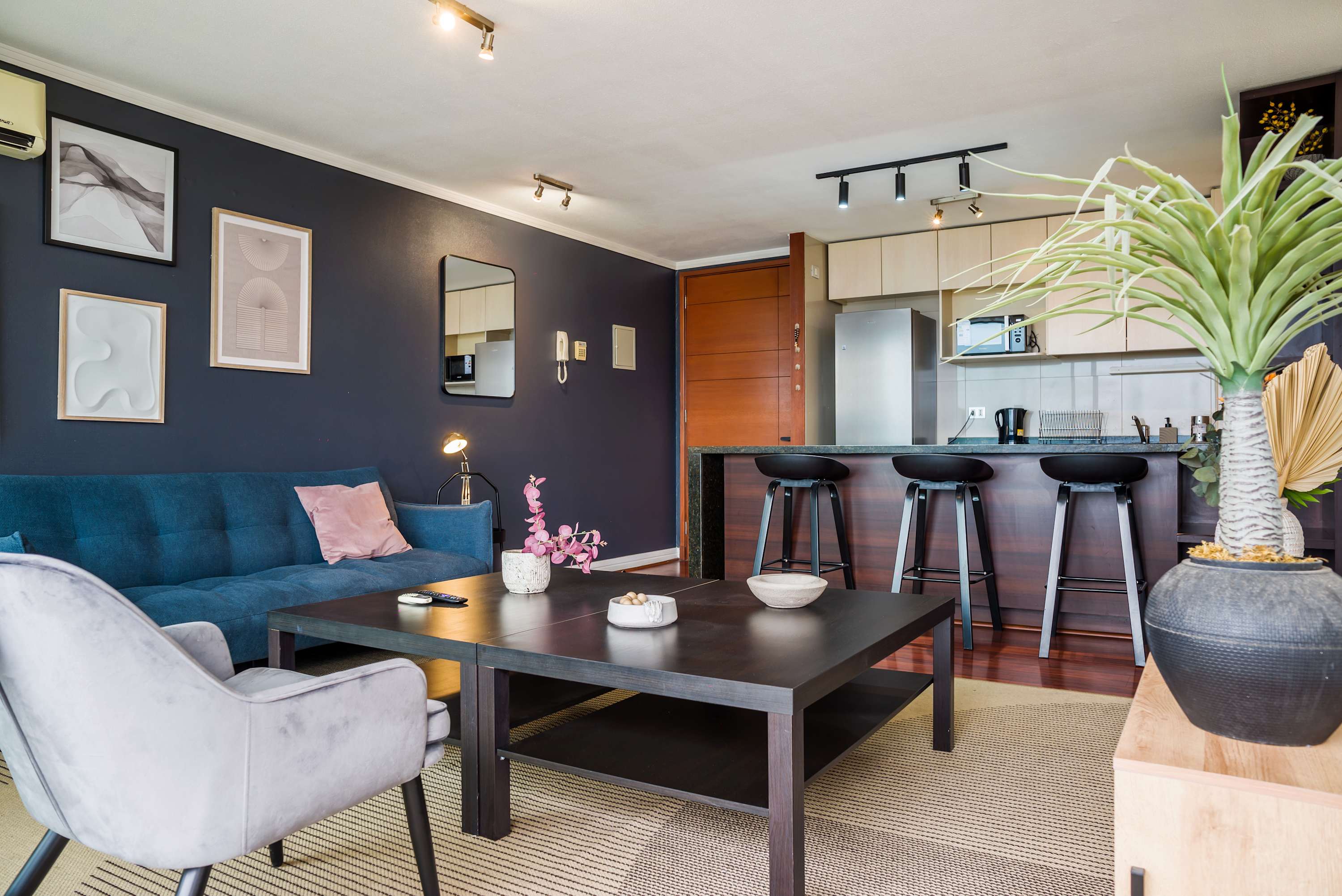 Private living room with a teal sofa, statement artwork, and an open kitchen island with three bar stools.