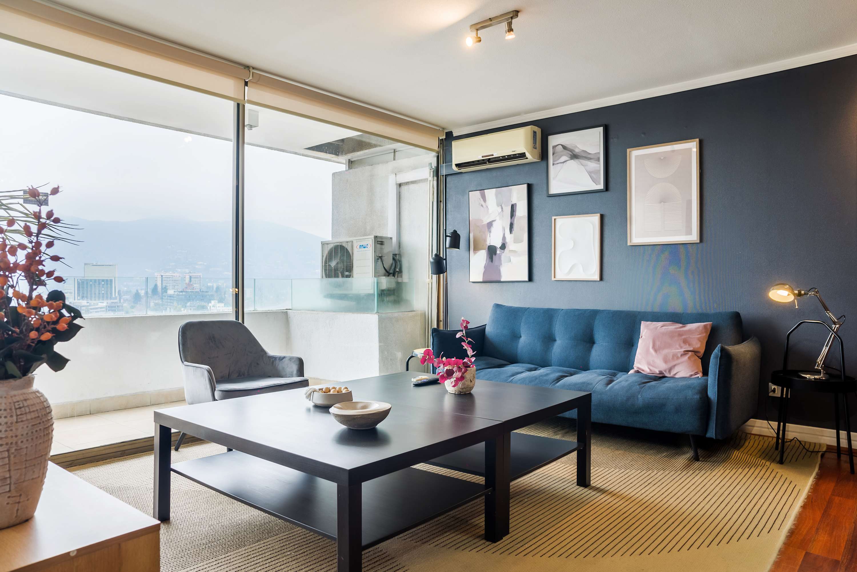 Private living room with a deep blue sectional, contemporary artwork, and expansive windows overlooking the city and mountains.