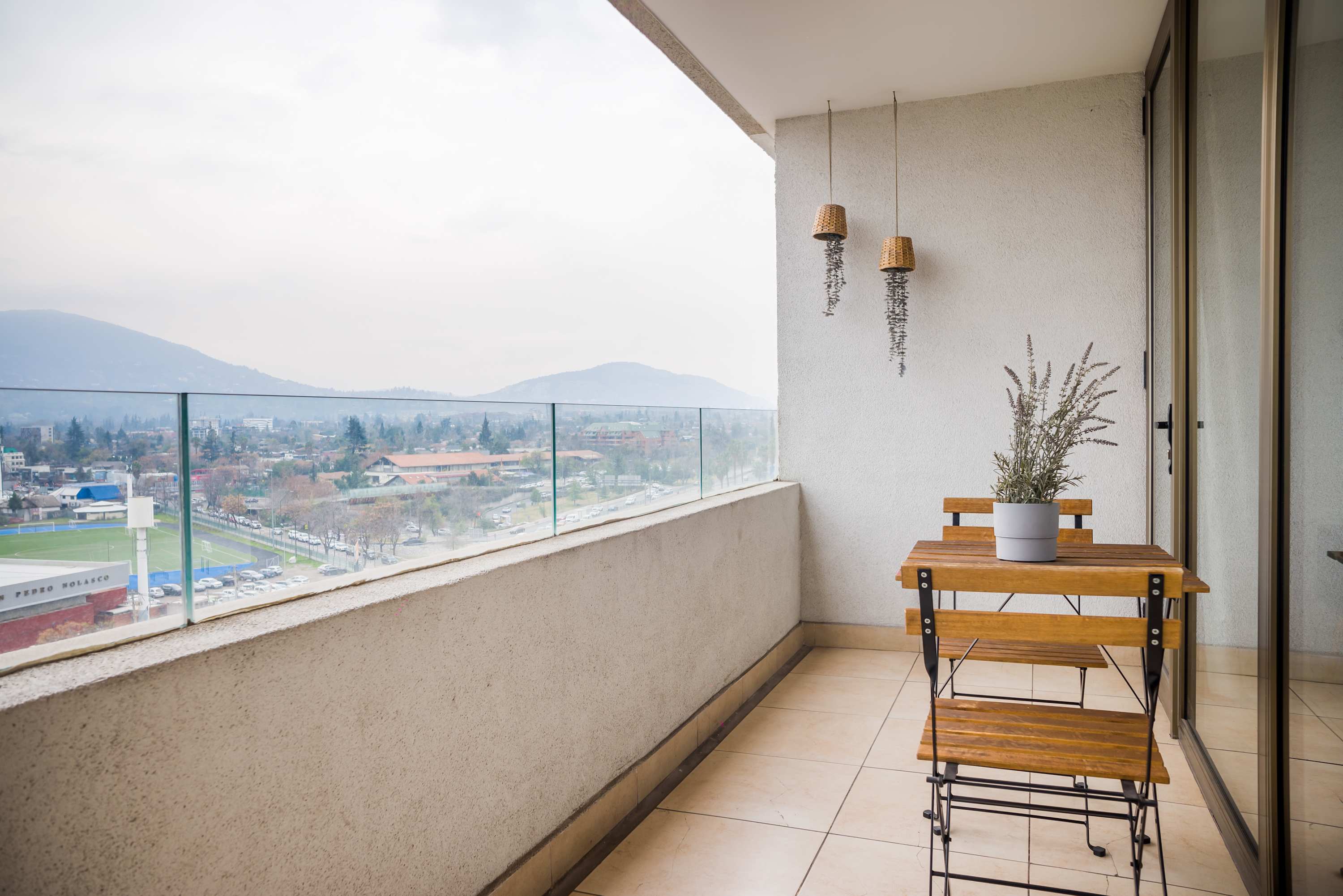 Private balcony with two wooden chairs, a potted plant, and sweeping mountain and city views beyond the glass railing.