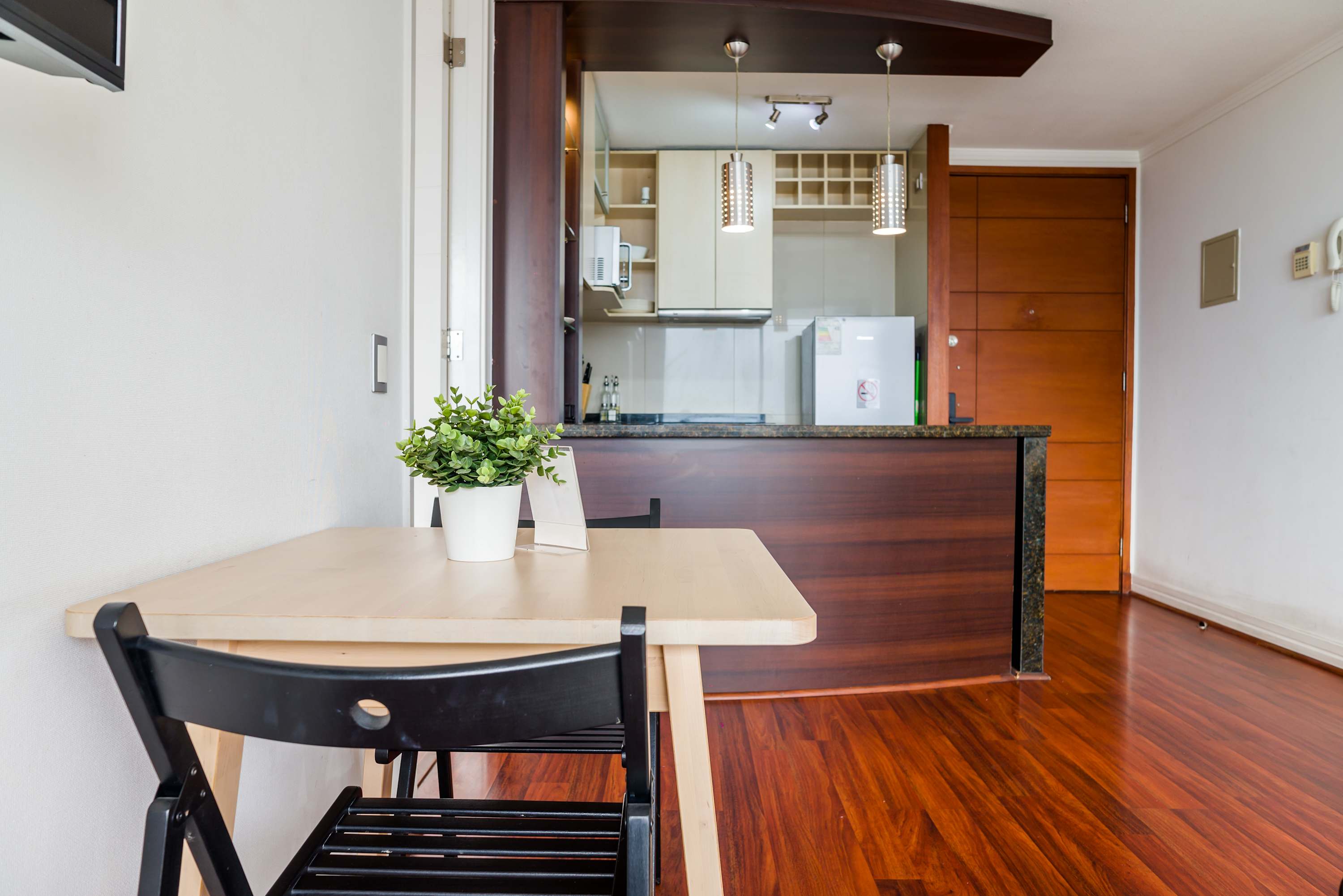 Private dining area with a light wood table, black chairs, and a compact modern kitchenette illuminated by distinctive pendant lights.