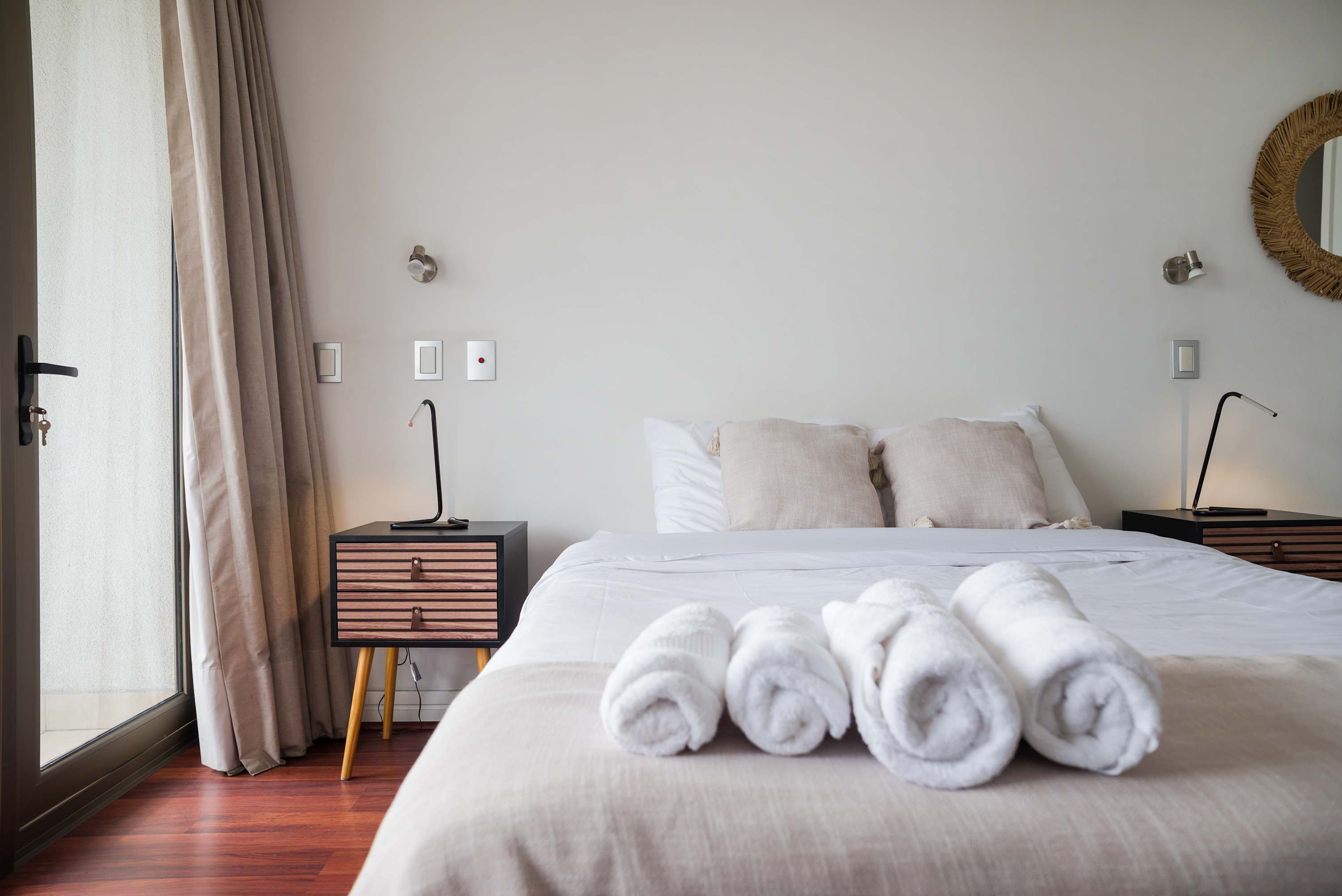 Private bedroom with crisp white linens, rolled towels, matching bedside reading lamps, and soft daylight through the glass door.