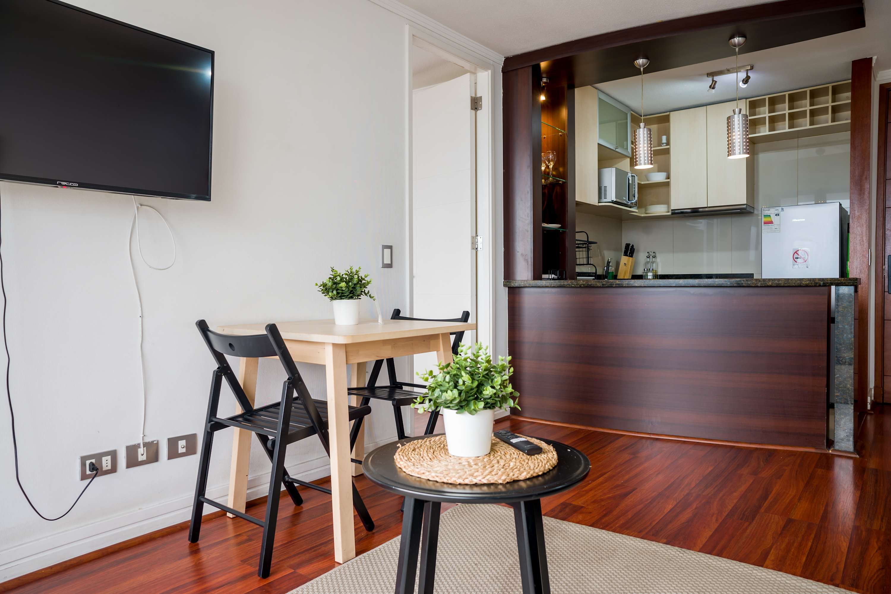 Private studio living room with a compact three-seat dining area, pendant lighting, open kitchen, and polished wood floors.