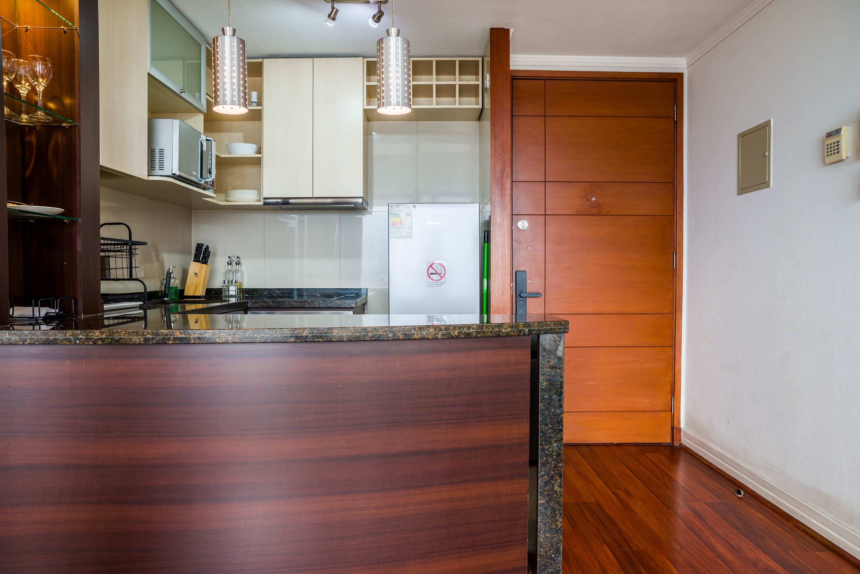 Compact studio kitchen with polished granite breakfast bar, pendant lighting, organized cabinetry, and essential cookware for easy in-home meals.