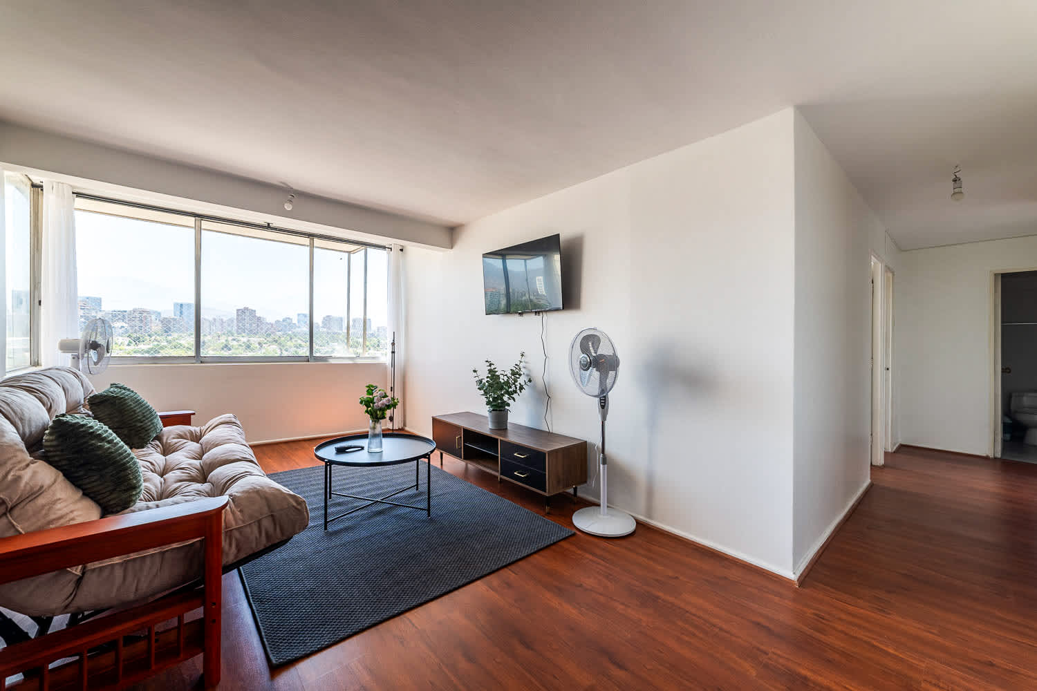 Private living room with a comfortable sofa, warm wood floors, and expansive windows overlooking Santiago’s skyline and greenery.