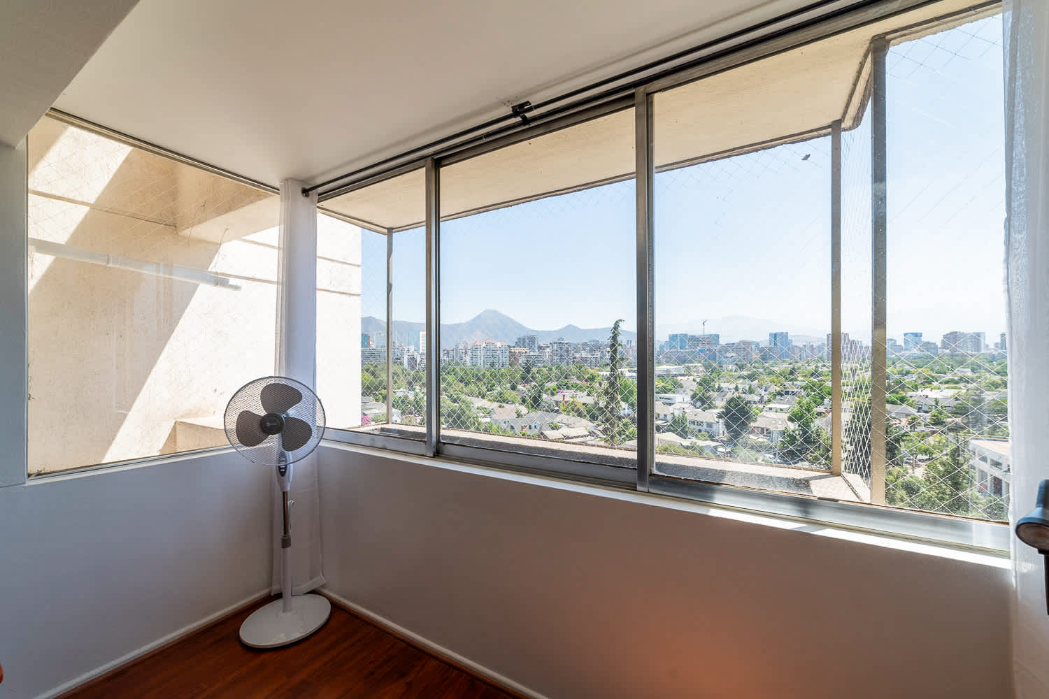 Enclosed balcony with panoramic city views, leafy neighborhoods, and mountain peaks beyond the windows.