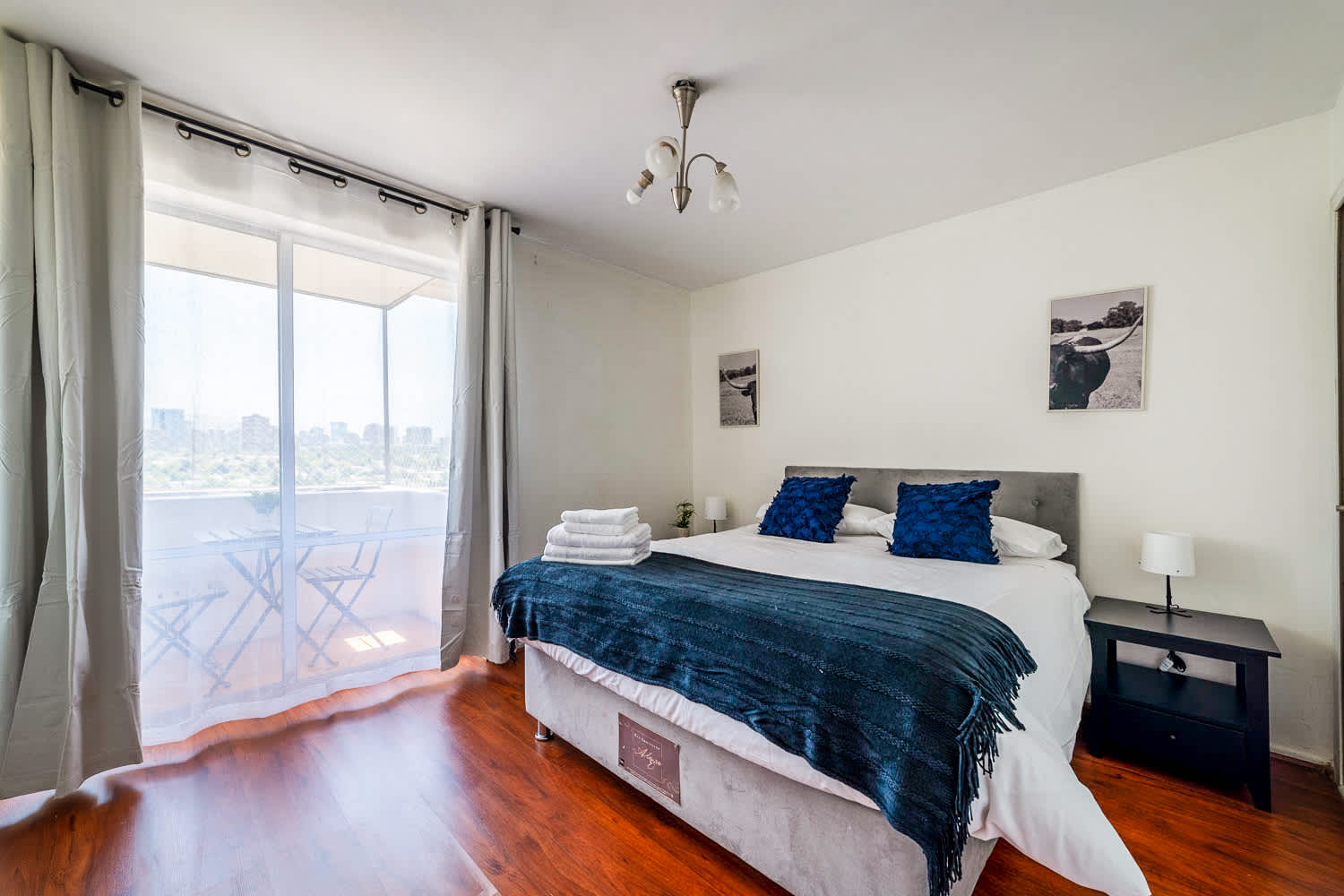 Serene bedroom with a king-size bed, navy accents, and a glass balcony overlooking the city skyline and greenery.