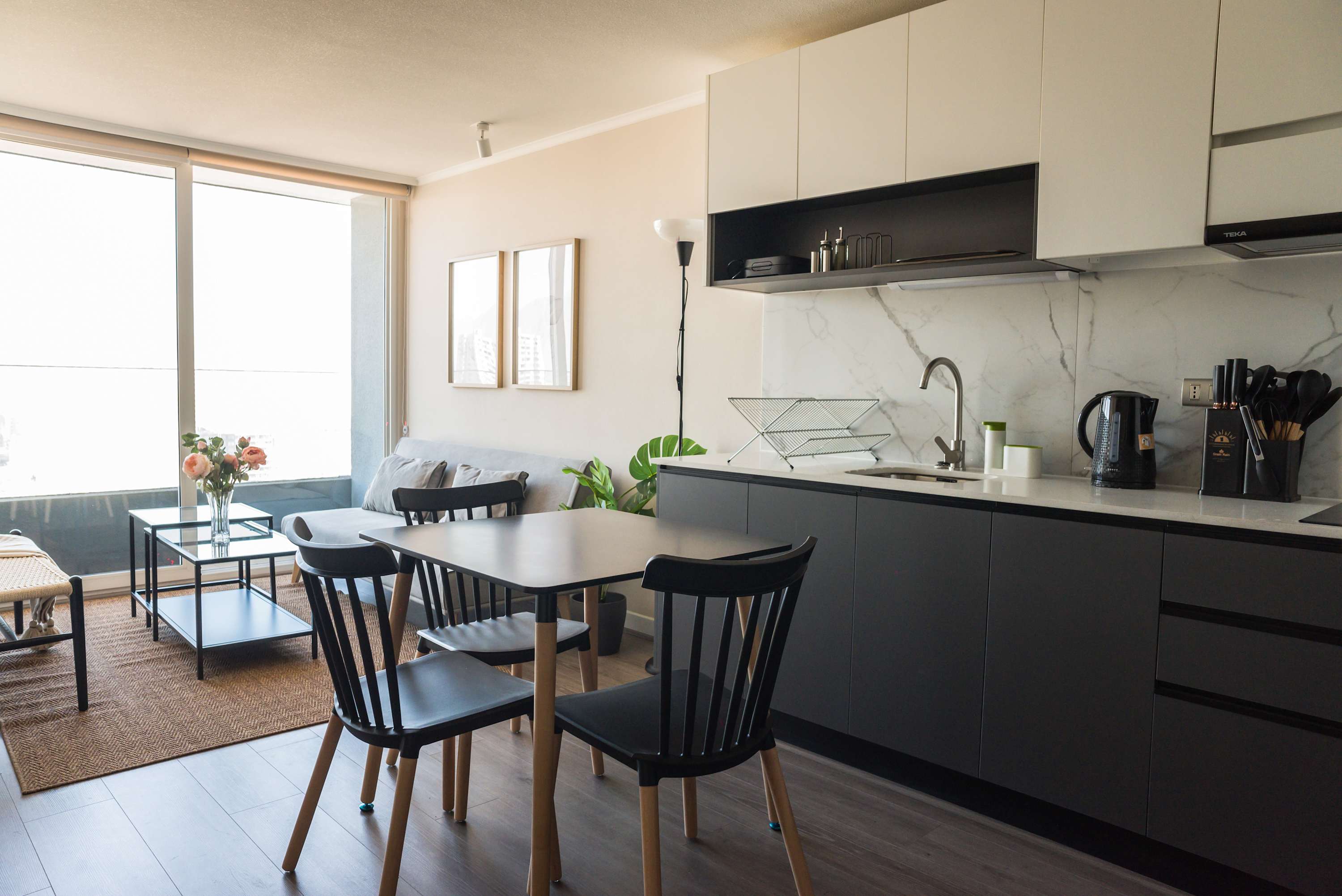 Open-plan kitchen and dining area with marble-look backsplash, modern appliances, and abundant natural light from the floor-to-ceiling windows.