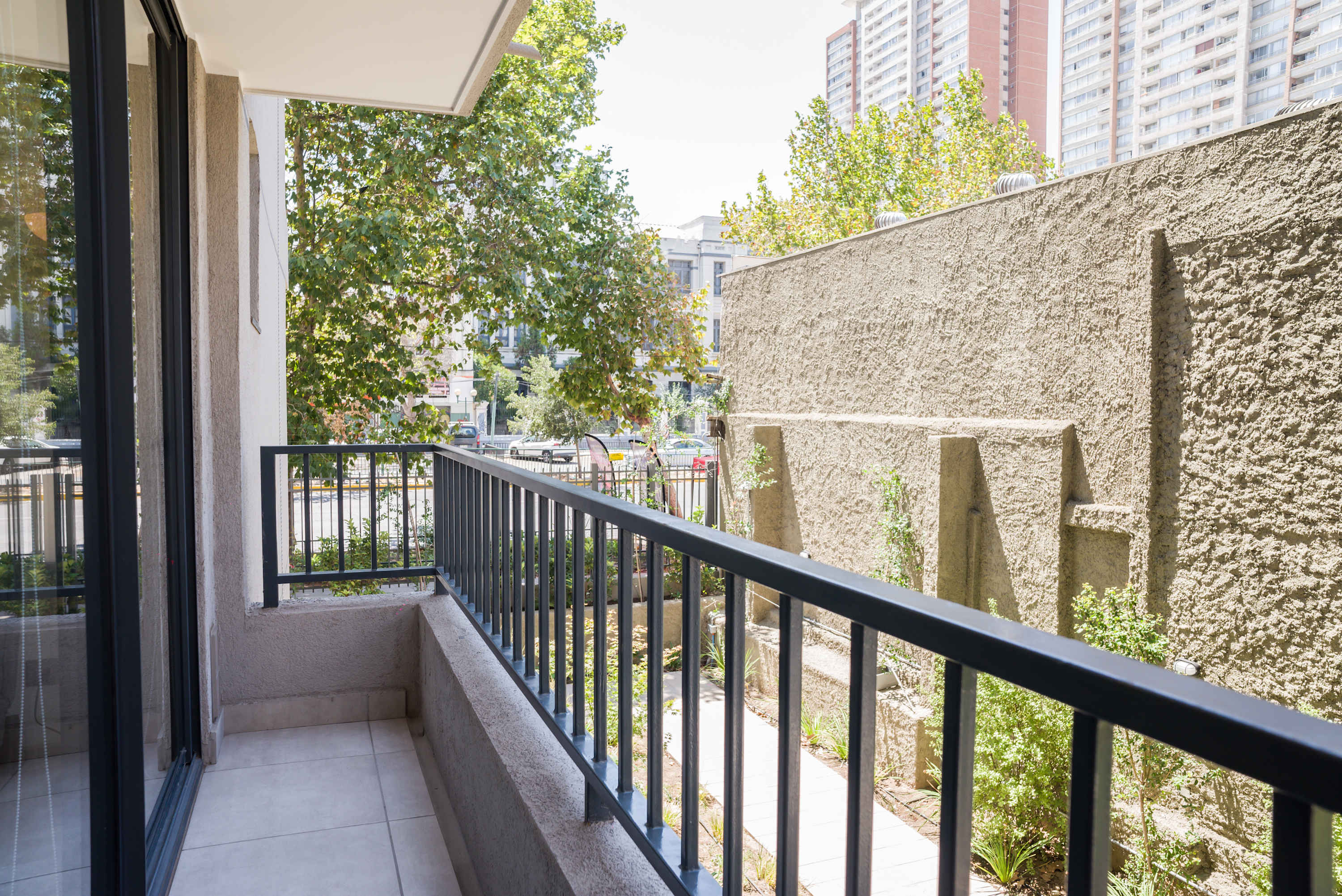 Private balcony with leafy surroundings, city views, and a secure black railing just off the apartment's sliding glass doors.