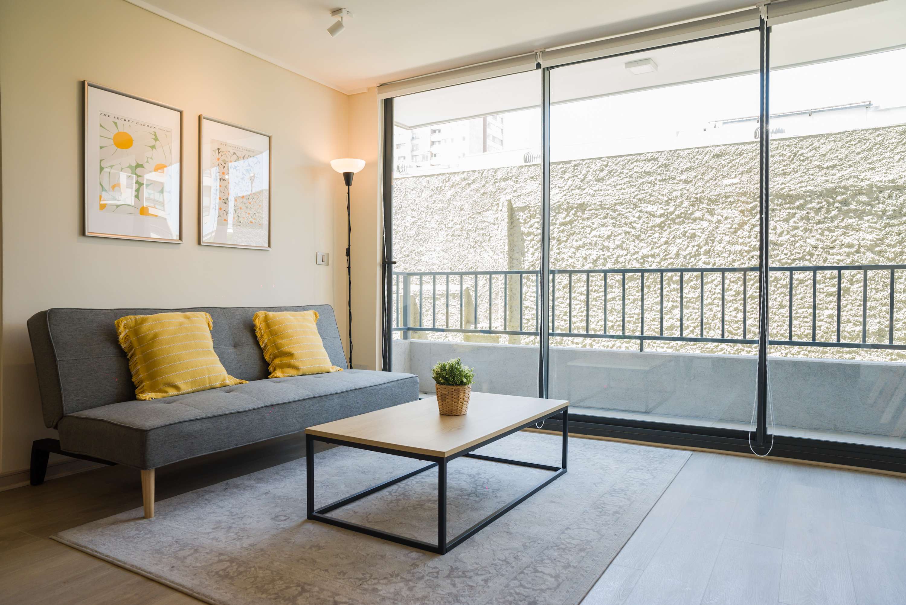 Living room with a gray sofa, mustard cushions, and full-height glass doors opening onto a private balcony.