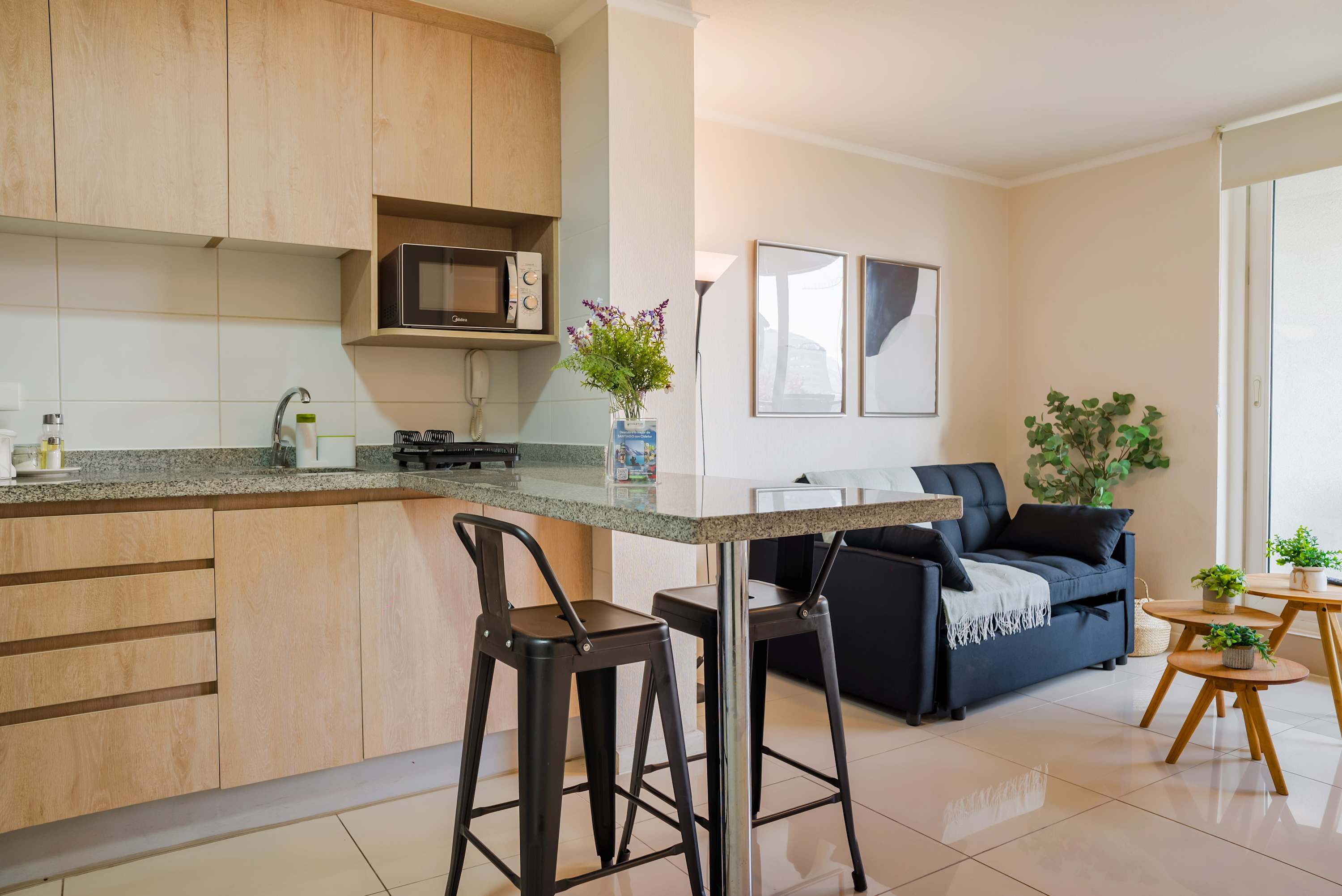 Open-plan kitchen with light wood cabinetry and a granite breakfast bar overlooking the cozy navy sofa area.
