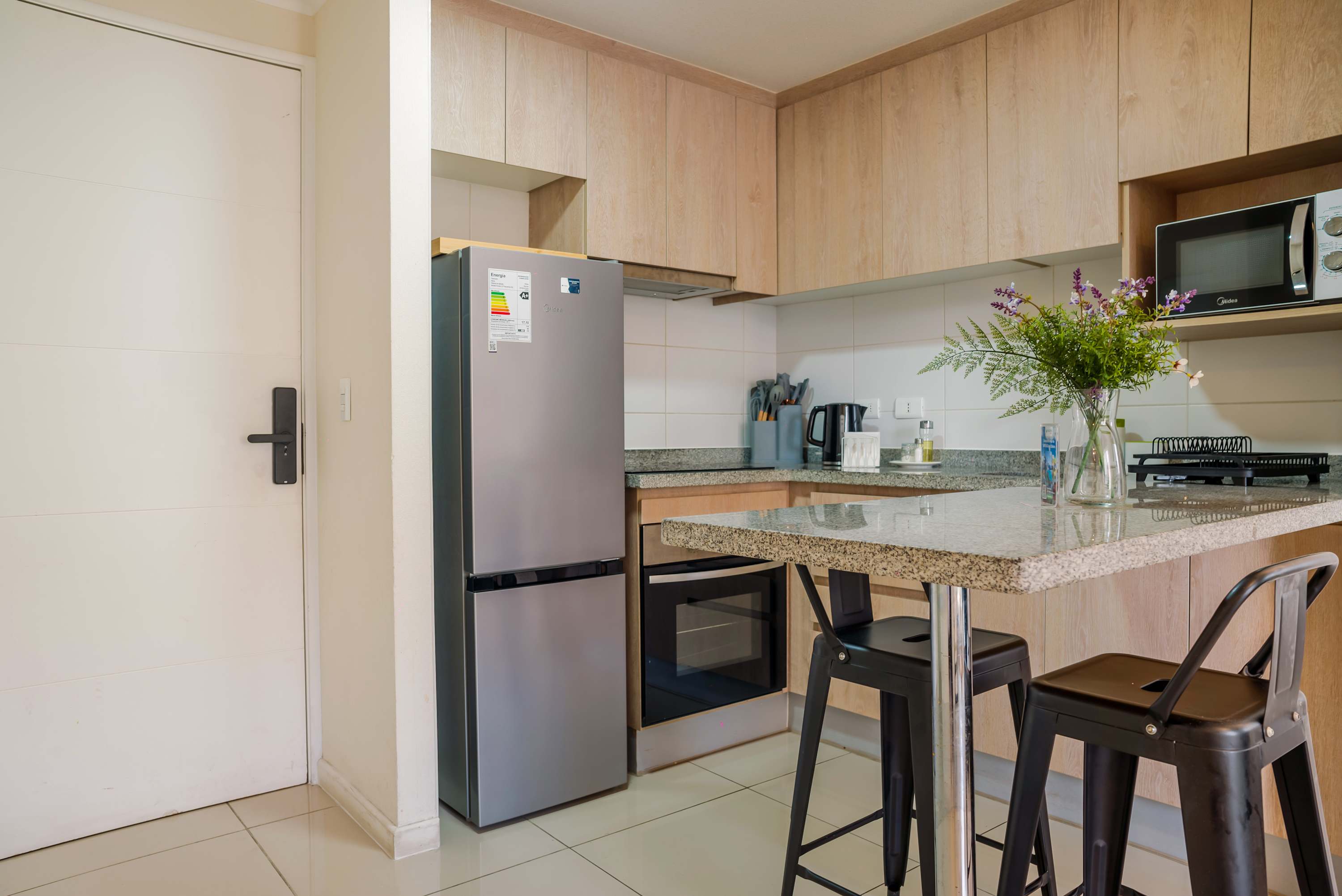 Private kitchen with light wood cabinetry, full-size appliances, and a granite breakfast bar with seating.