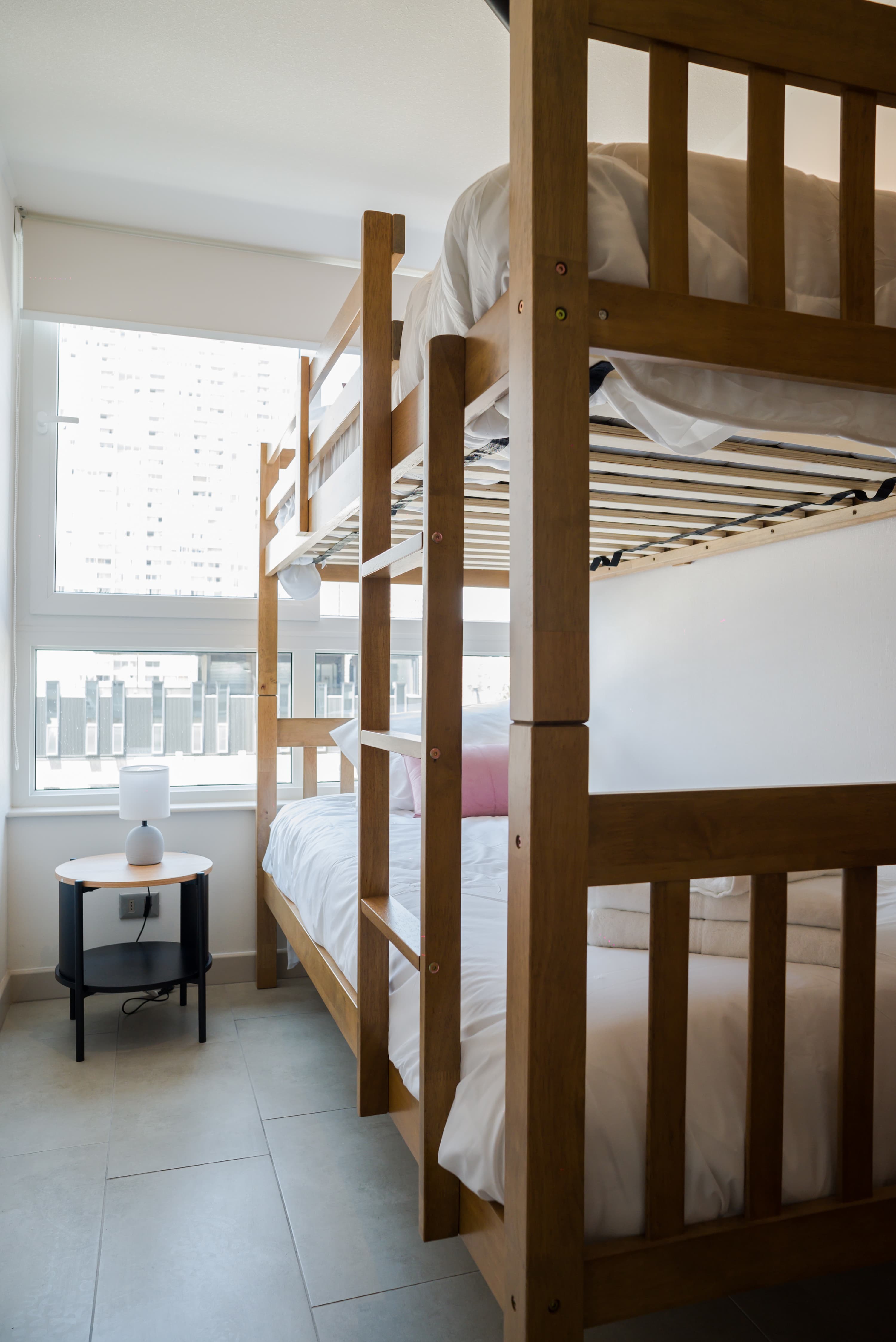 Private bedroom with a space-saving wooden bunk bed, crisp white bedding, and bright city views through large windows.