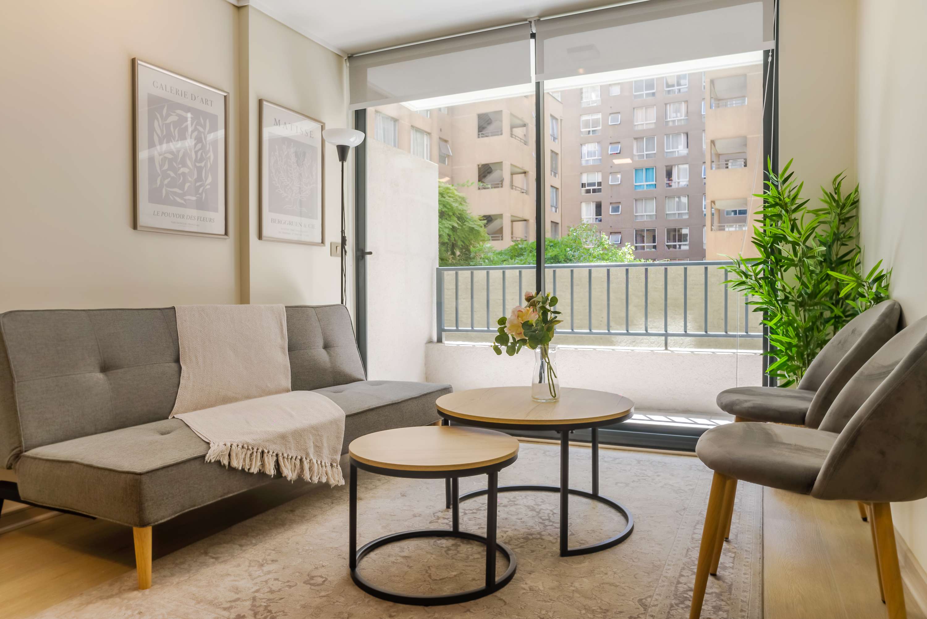Private living room with a gray sectional, layered coffee tables, botanical accents, and bright balcony access overlooking the surrounding greenery.