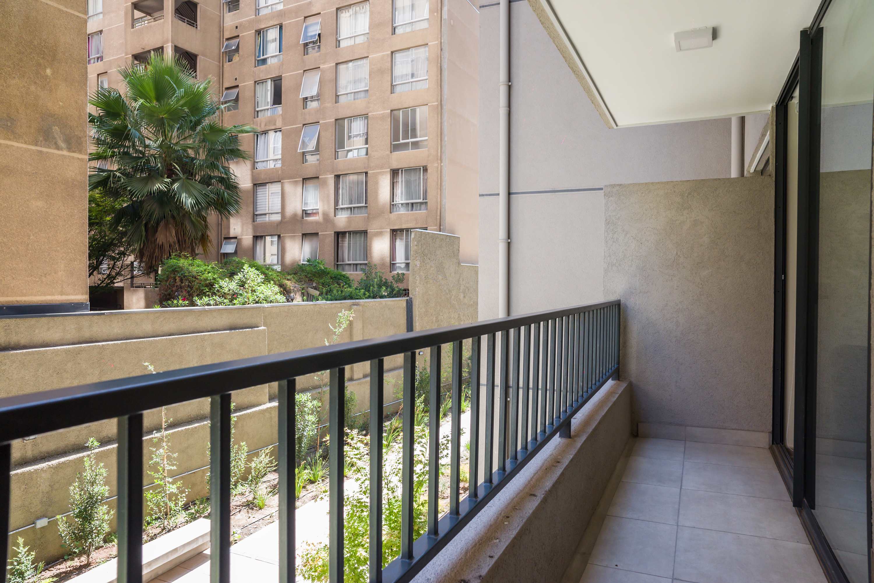 Private balcony overlooking a landscaped courtyard with palm trees and greenery, offering a bright outdoor spot just beyond the sliding glass doors.