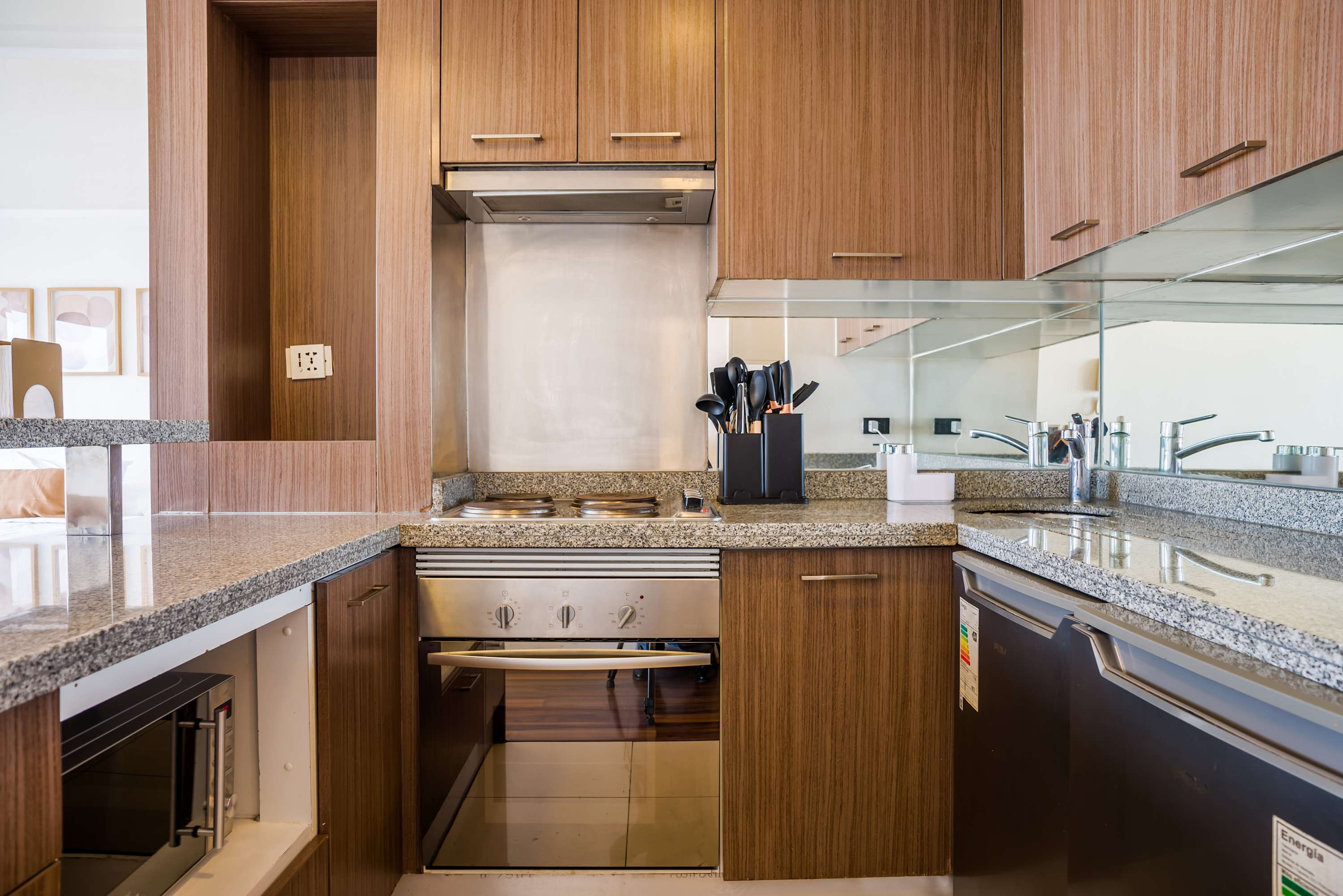 Compact studio kitchen with warm wood cabinetry, granite counters, mirrored backsplash, and full-size cooking appliances for convenient meals.