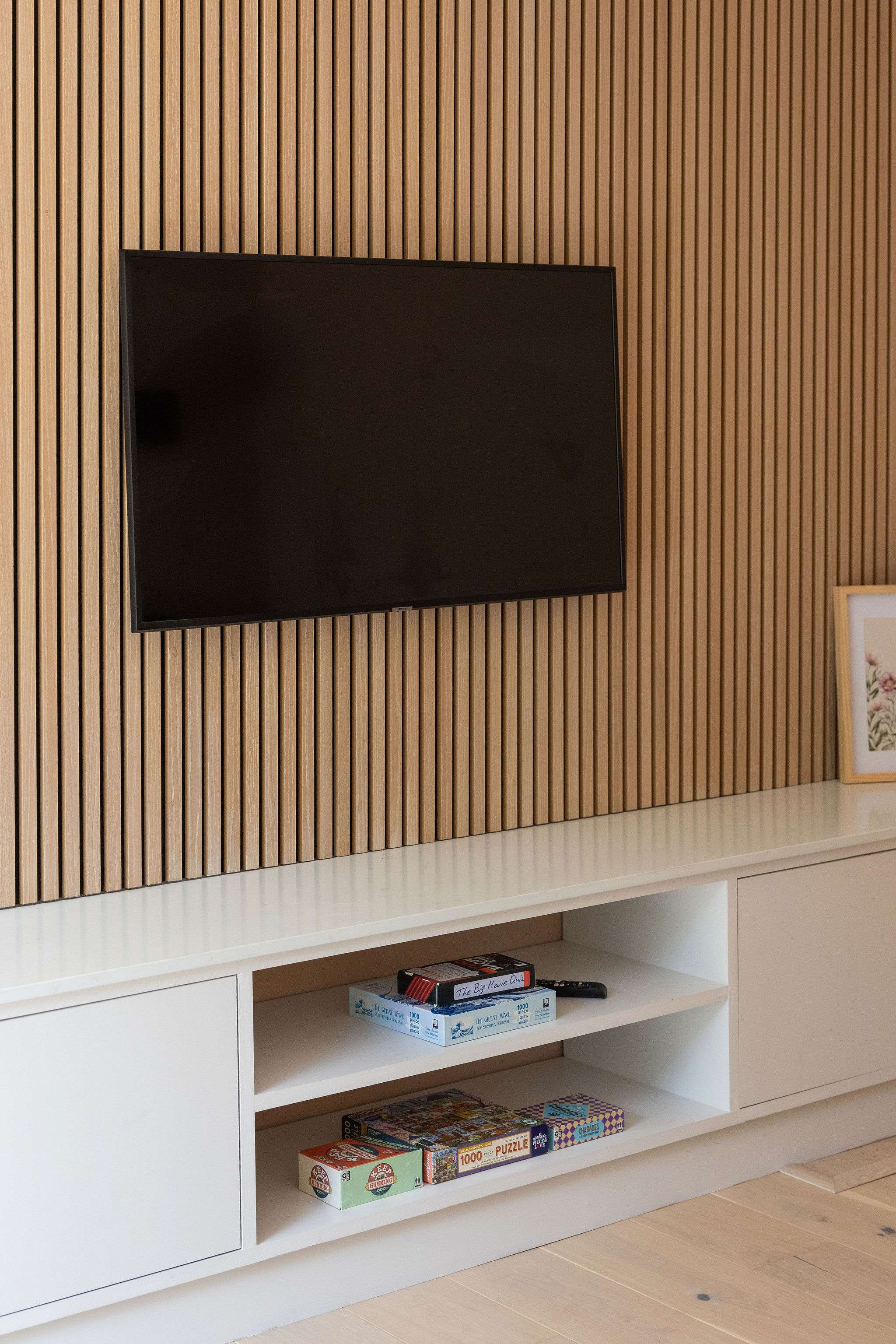 In the snug room a stylish media wall with warm timber slat detailing, a wall-mounted TV and sleek built-in storage, with a selection of games tucked below for relaxed nights in.