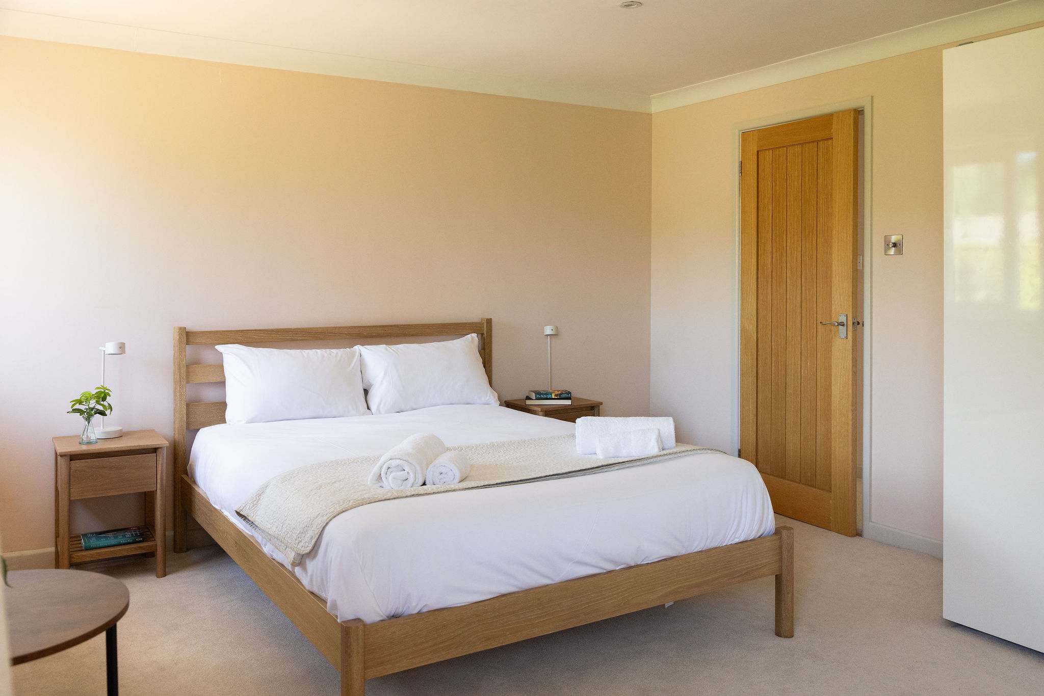 Spacious, light-filled master bedroom featuring a king-size bed, warm natural wood furniture, soft neutral tones, generous wardrobe storage, a dedicated dressing table, contemporary artwork and windows on two sides bringing in plenty of natural light