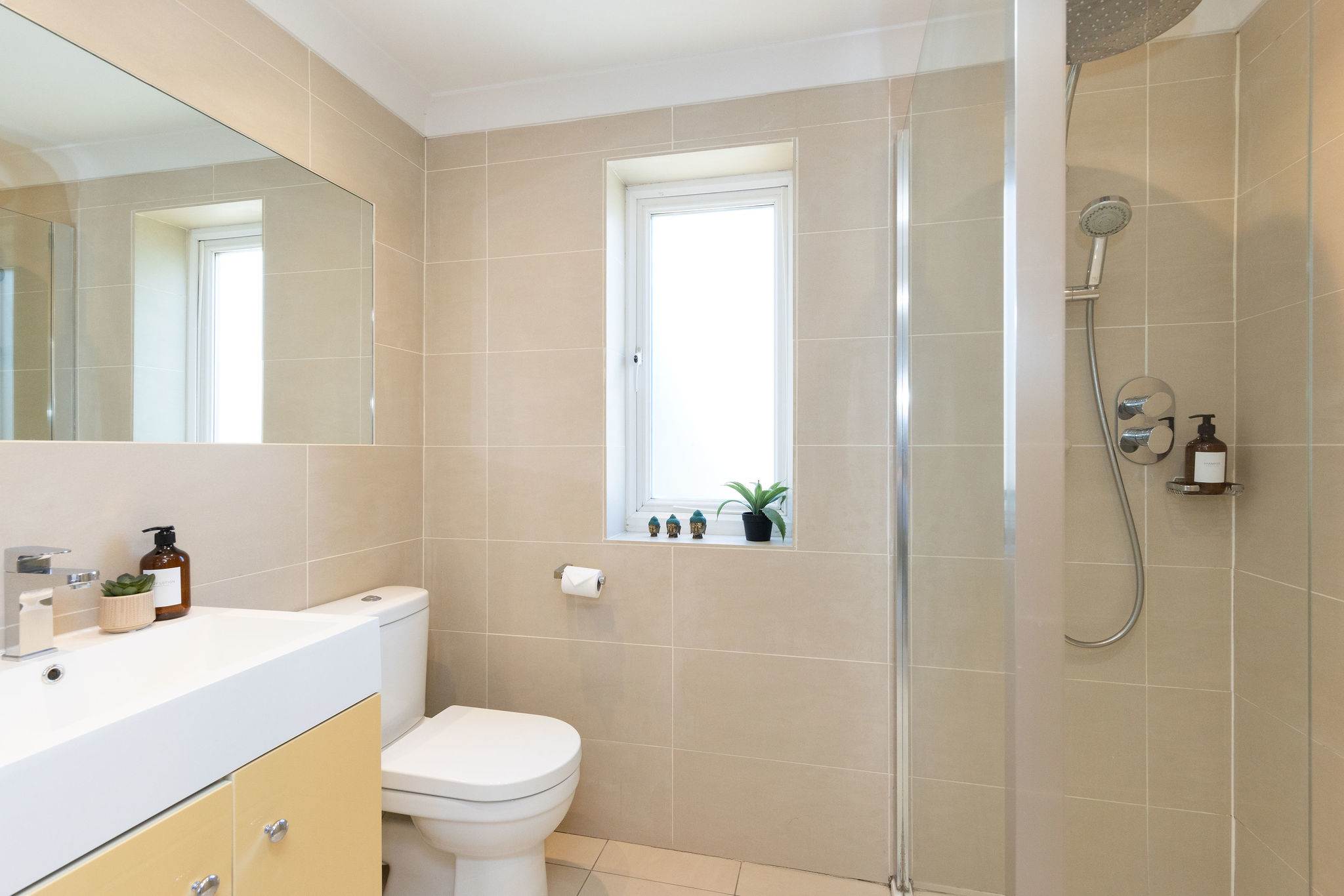 Clean-lined and contemporary, this spacious shower room pairs warm neutral tiling with a large walk-in shower, generous vanity unit and plenty of natural light.
