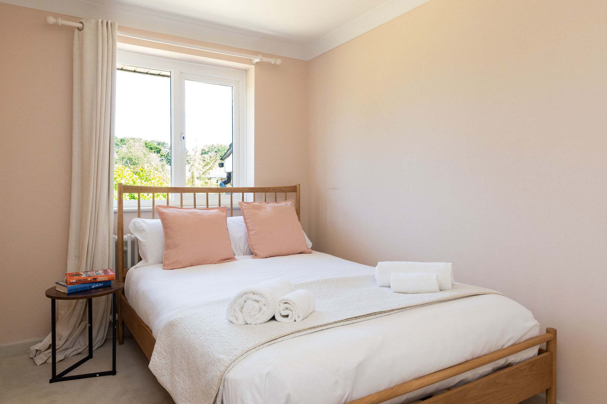 Soft blush tones, crisp white bedding and warm natural finishes give this double bedroom a calm, restful feel, with plenty of daylight coming through the window.