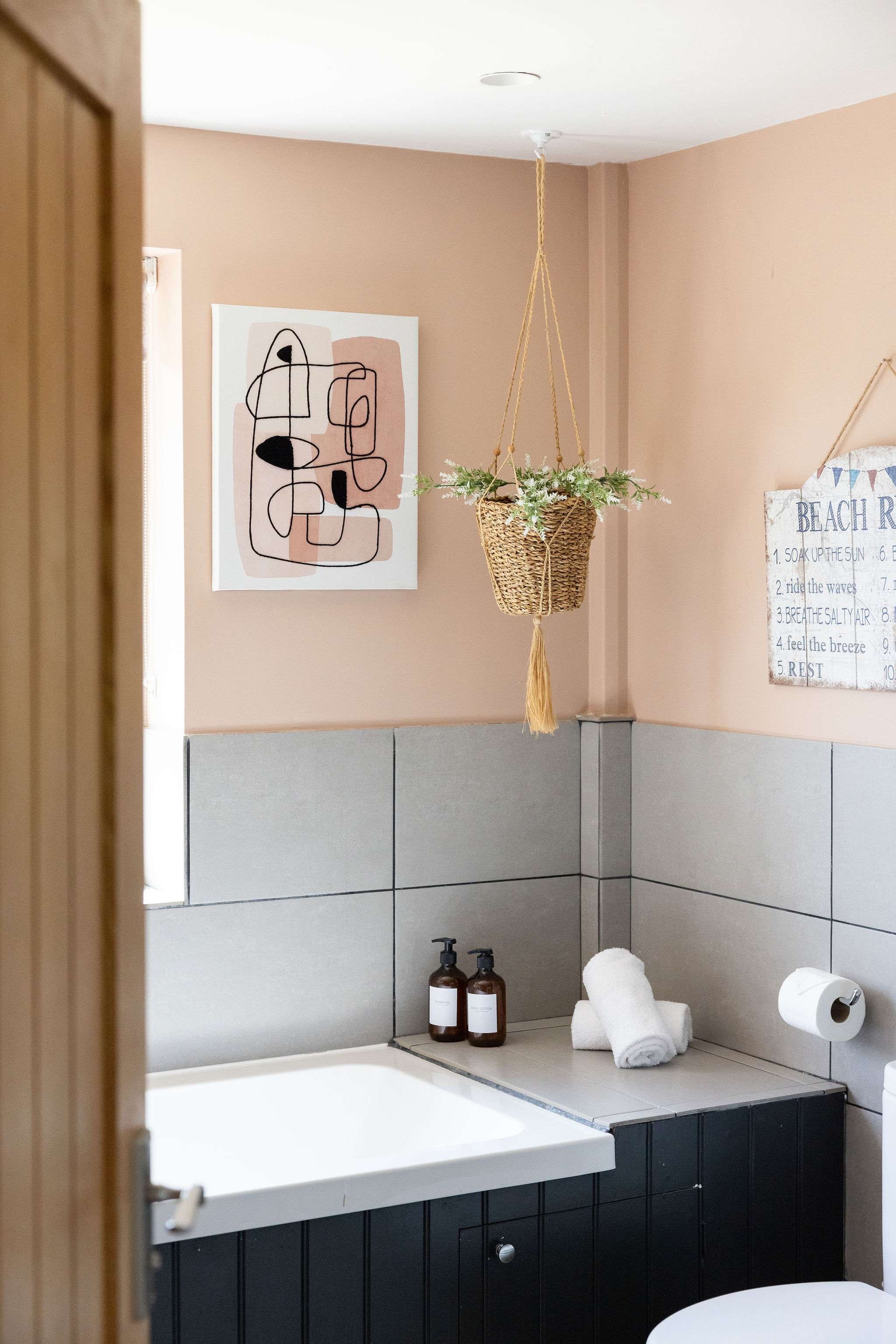 It’s the little details that make this shower room stand out — from the hanging woven basket and soft greenery to the blush walls, dark vanity and neatly styled essentials.