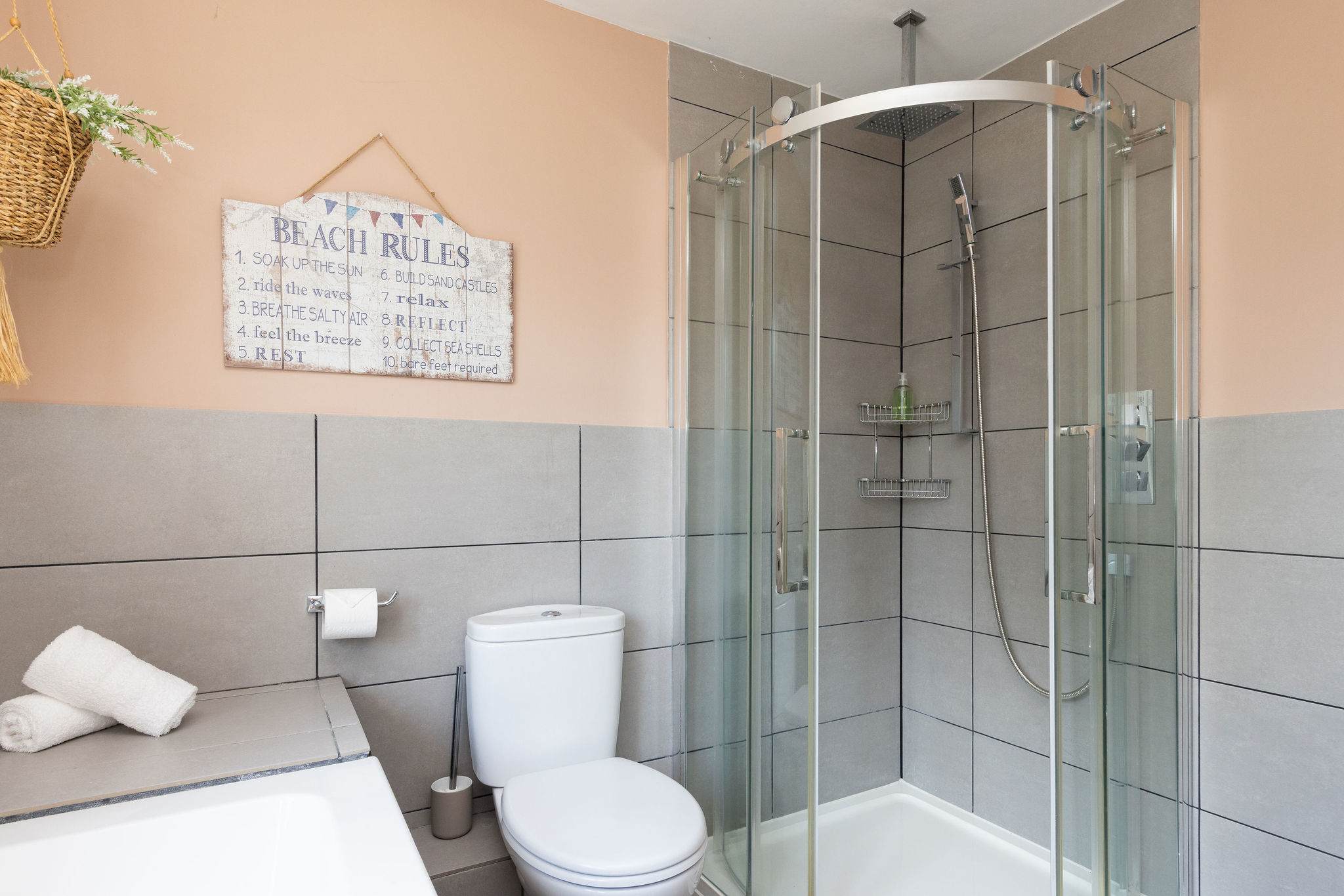 Soft blush walls and contemporary grey tiling give this shower room a fresh, stylish feel, with a glass-enclosed corner shower, WC, wide countertop and neatly arranged finishing touches.