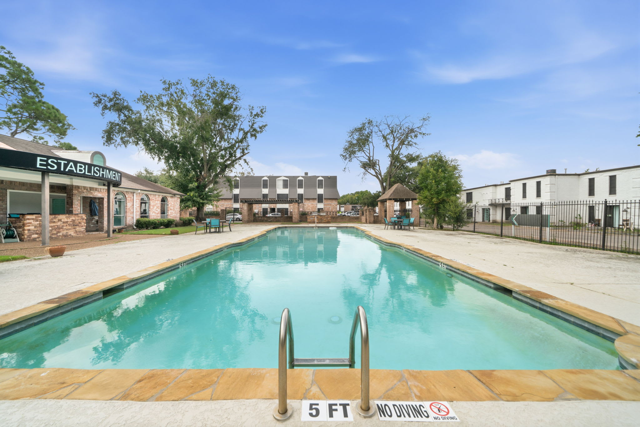 Community pool with turquoise water, shaded gazebo seating, and a spacious deck for sunny days by the water.