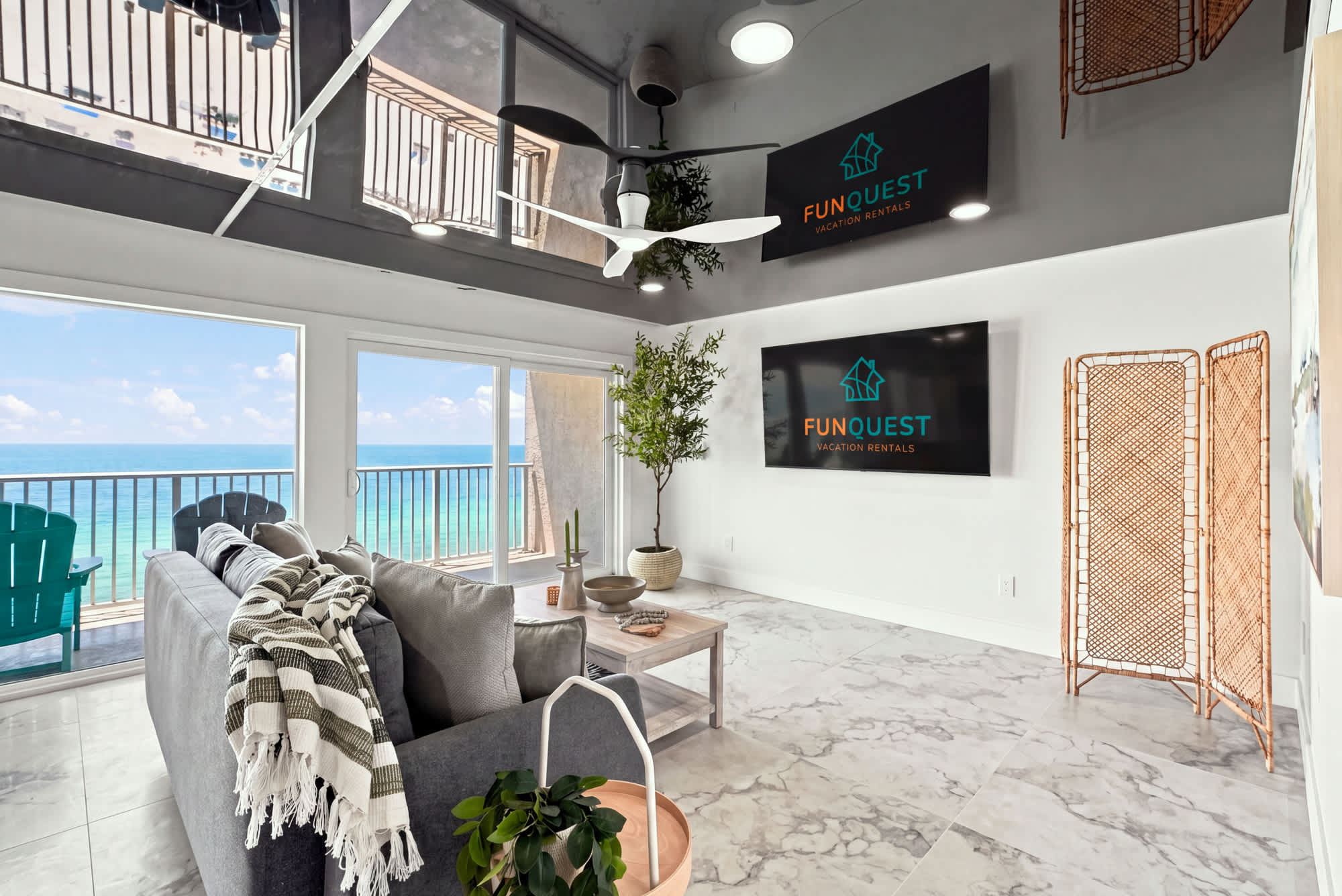 The Summit 1512 – Living room with ocean view, gray sofa, and two wall-mounted TVs.