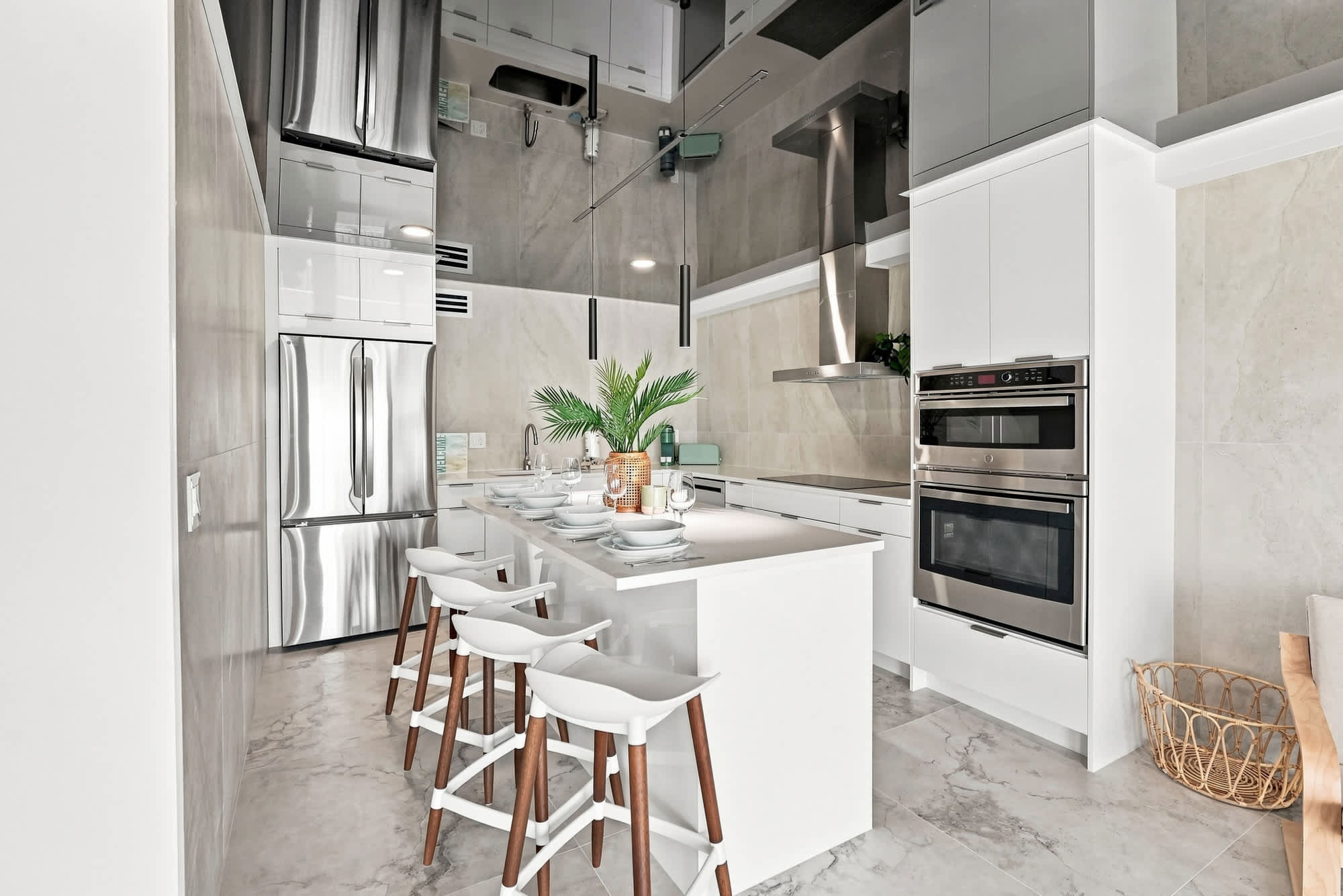 The Summit 1512 – Modern kitchen with stainless steel appliances, white cabinets, marble flooring, and a central island with seating.