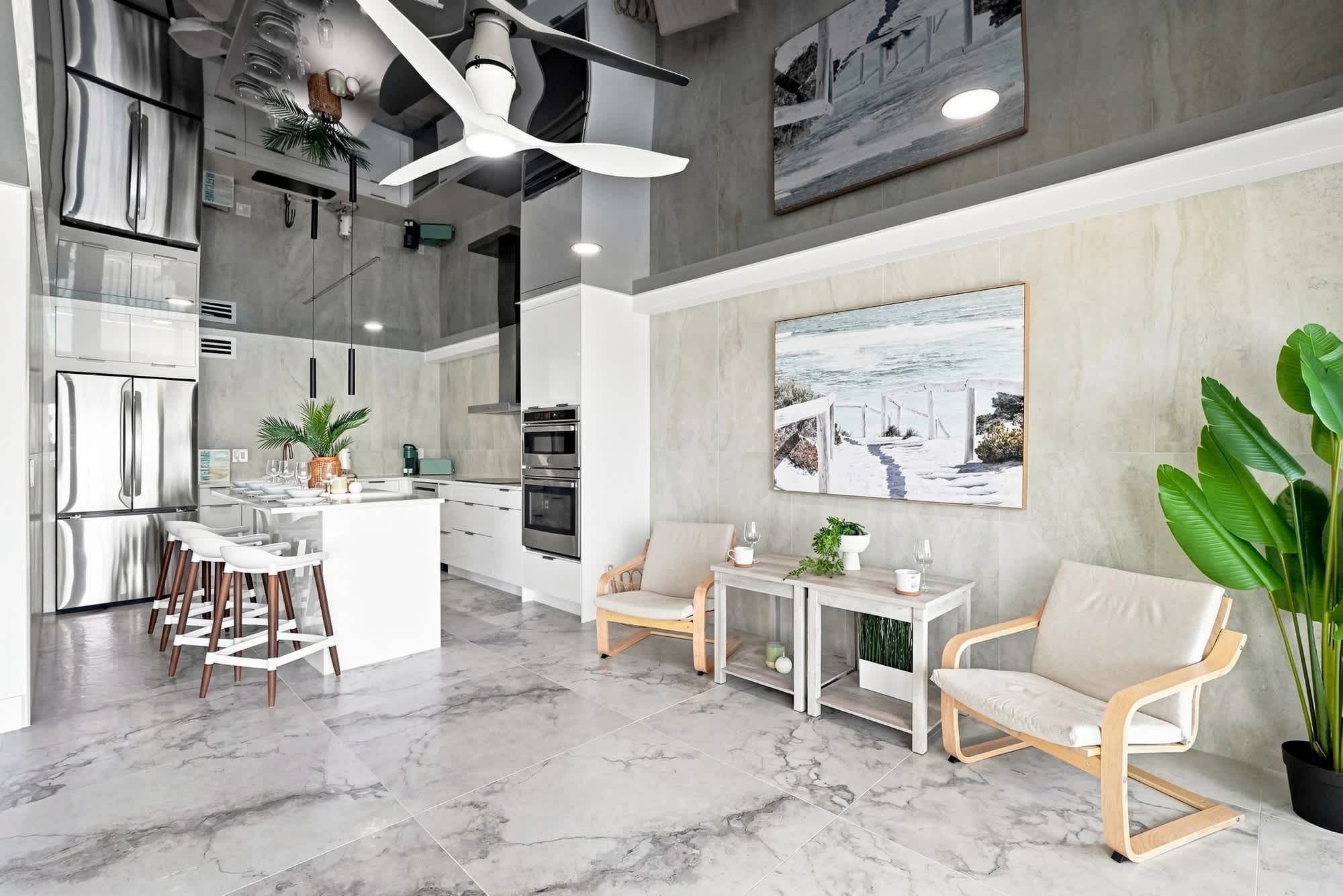The Summit 1512 – Modern kitchen and living area with marble floors, island seating, and artwork depicting a beach scene.