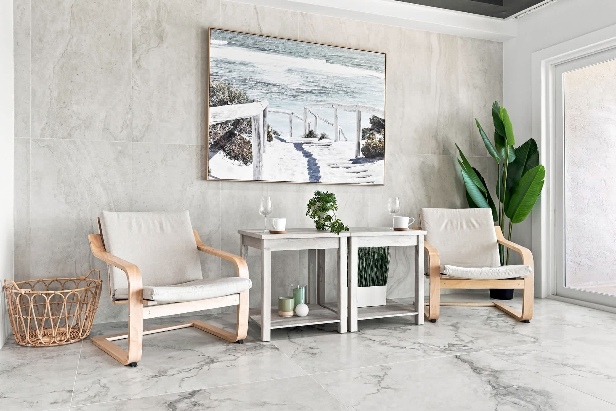 The Summit 1512 – Living area with two beige chairs, a table, and a painting of a beach scene.