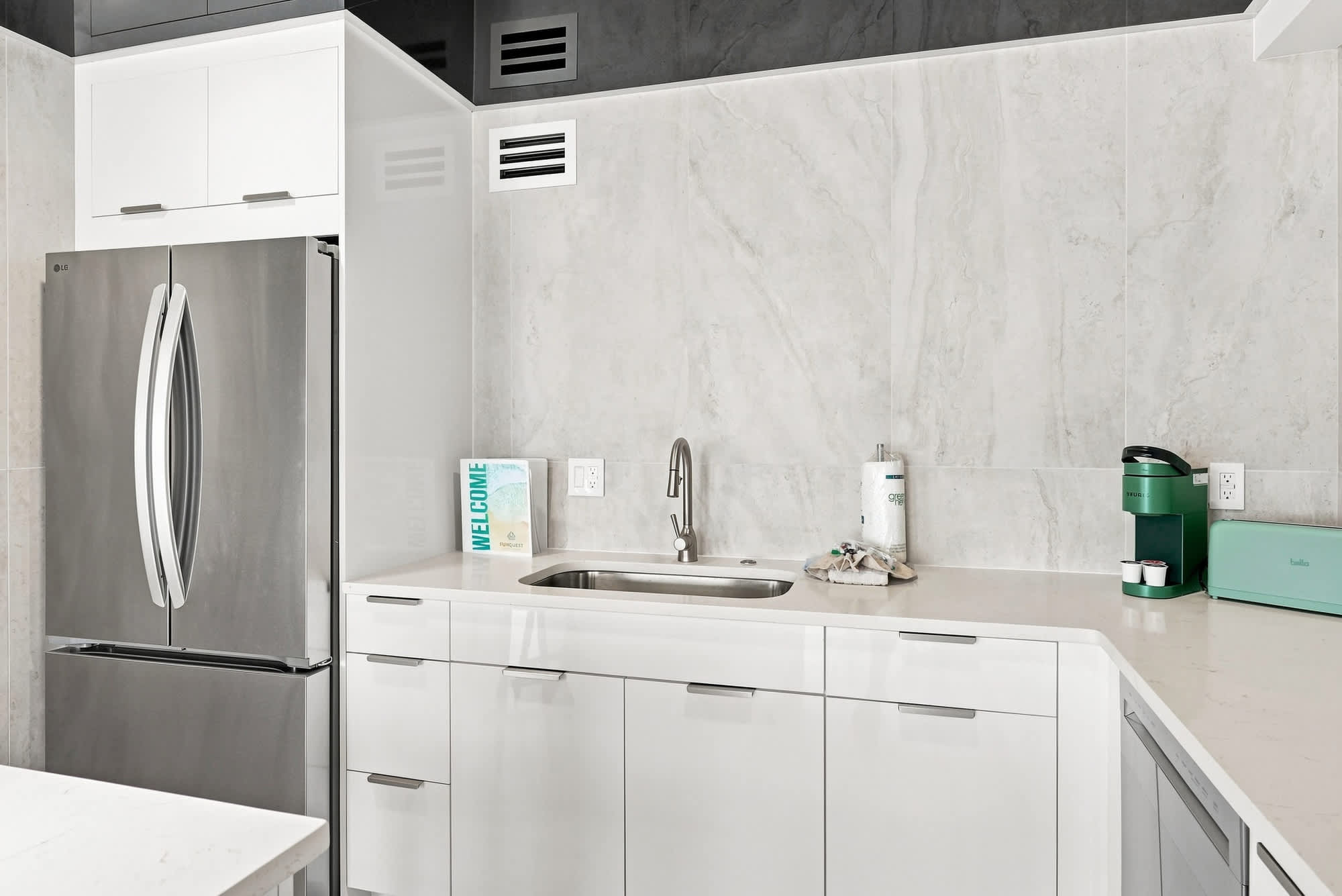 The Summit 1512 – Modern kitchen with stainless steel refrigerator, sink, and coffee maker on a light countertop.