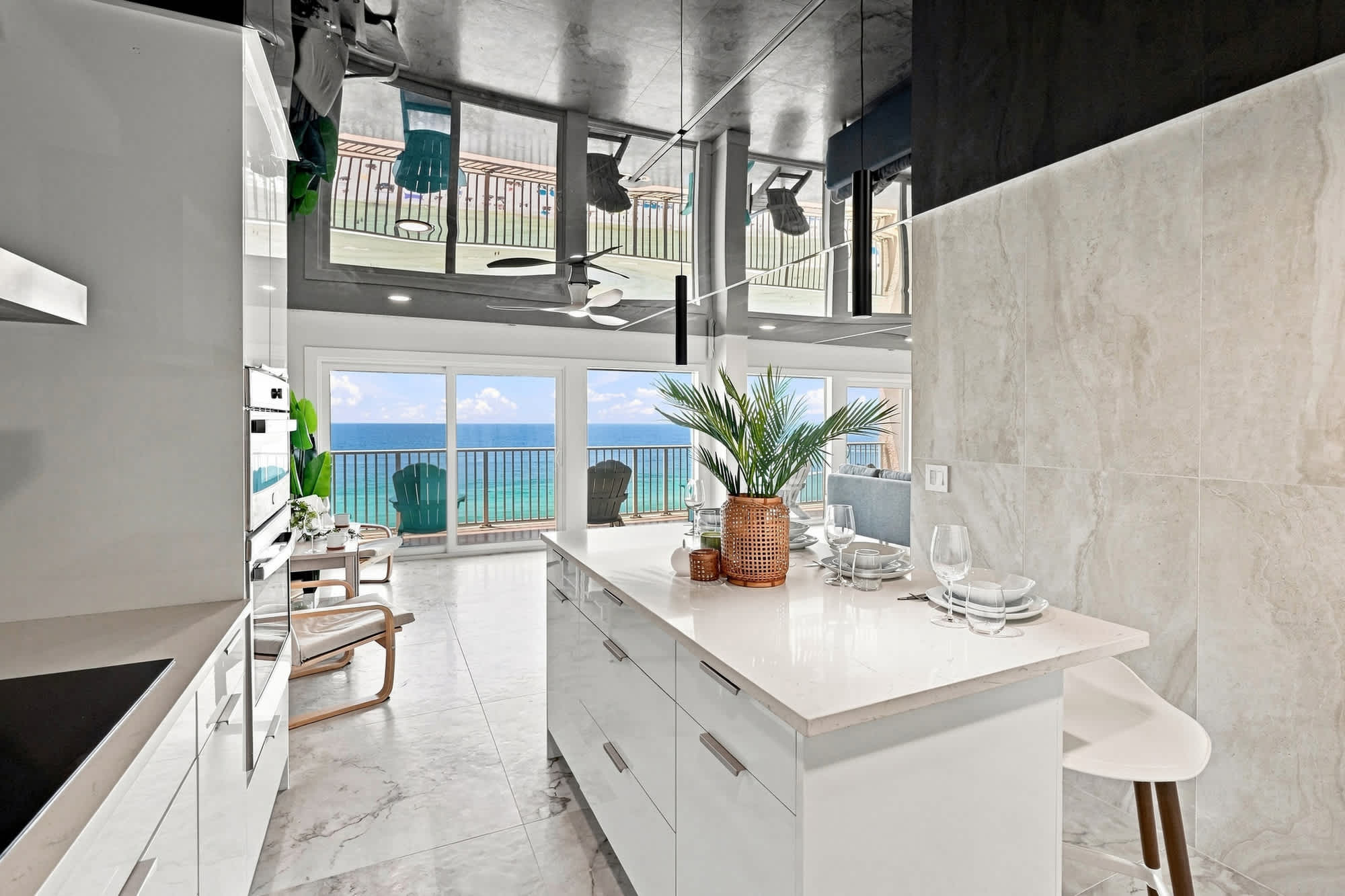 The Summit 1512 – Modern kitchen with white cabinetry, ocean view, and access to a balcony with lounge chairs.