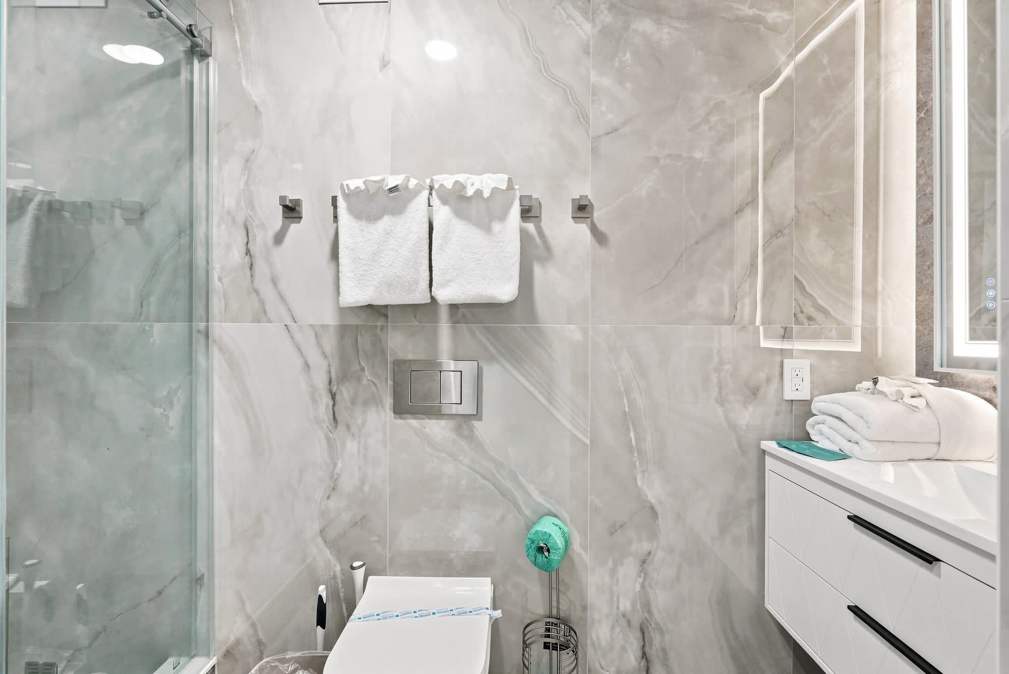 The Summit 1512 – Modern bathroom featuring marble walls, glass shower, towel rack, and stylish sink with storage below.