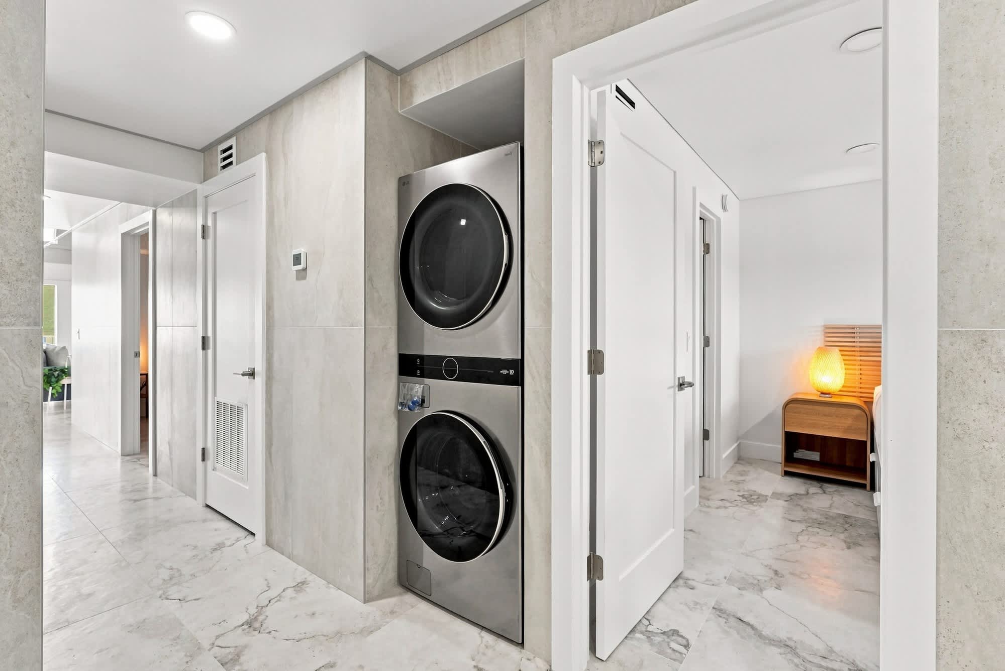 The Summit 1512 – Laundry area featuring stacked washer and dryer, marble flooring, and white hallway with doors.