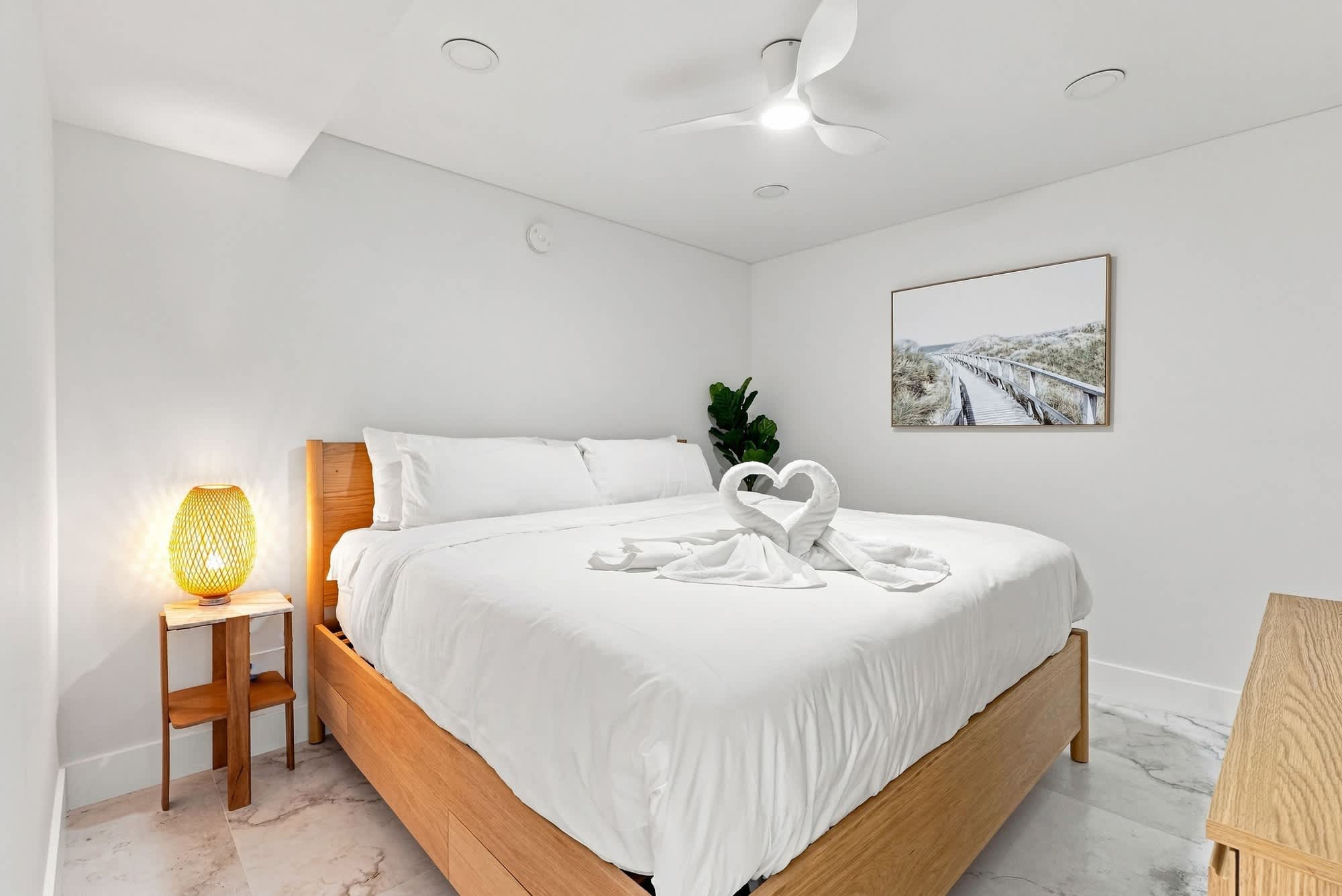The Summit 1512 – Bedroom with a large bed, decorative towel swans, and a plant, featuring a lighted side table and wall art.