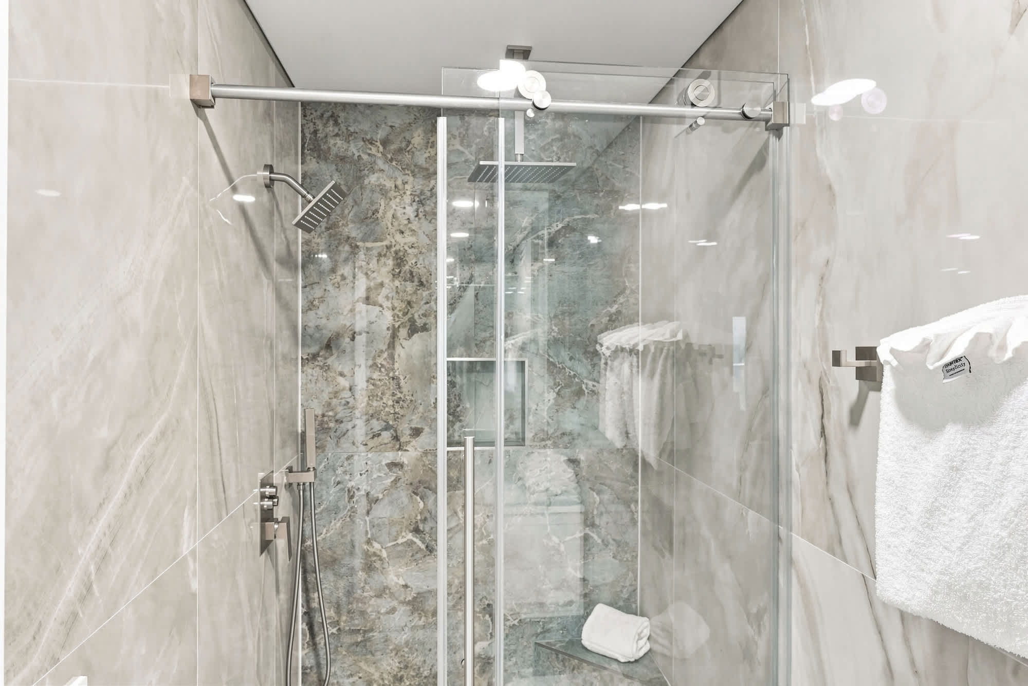 The Summit 1512 – Modern shower with glass doors, marble walls, rainfall showerhead, and neatly arranged towels.
