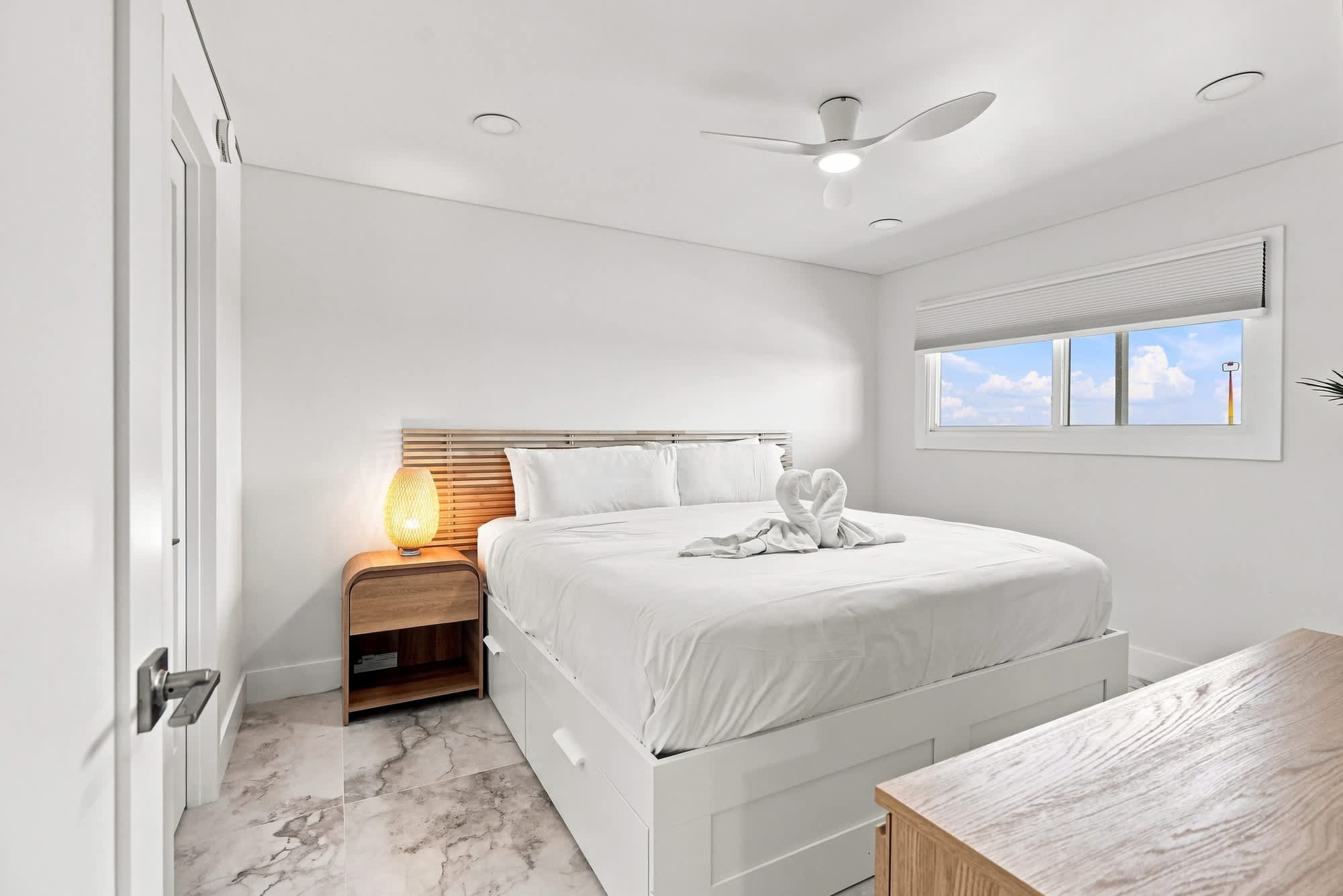 The Summit 1512 – Bright bedroom with a king-sized bed, bedside table, fan, and window view.