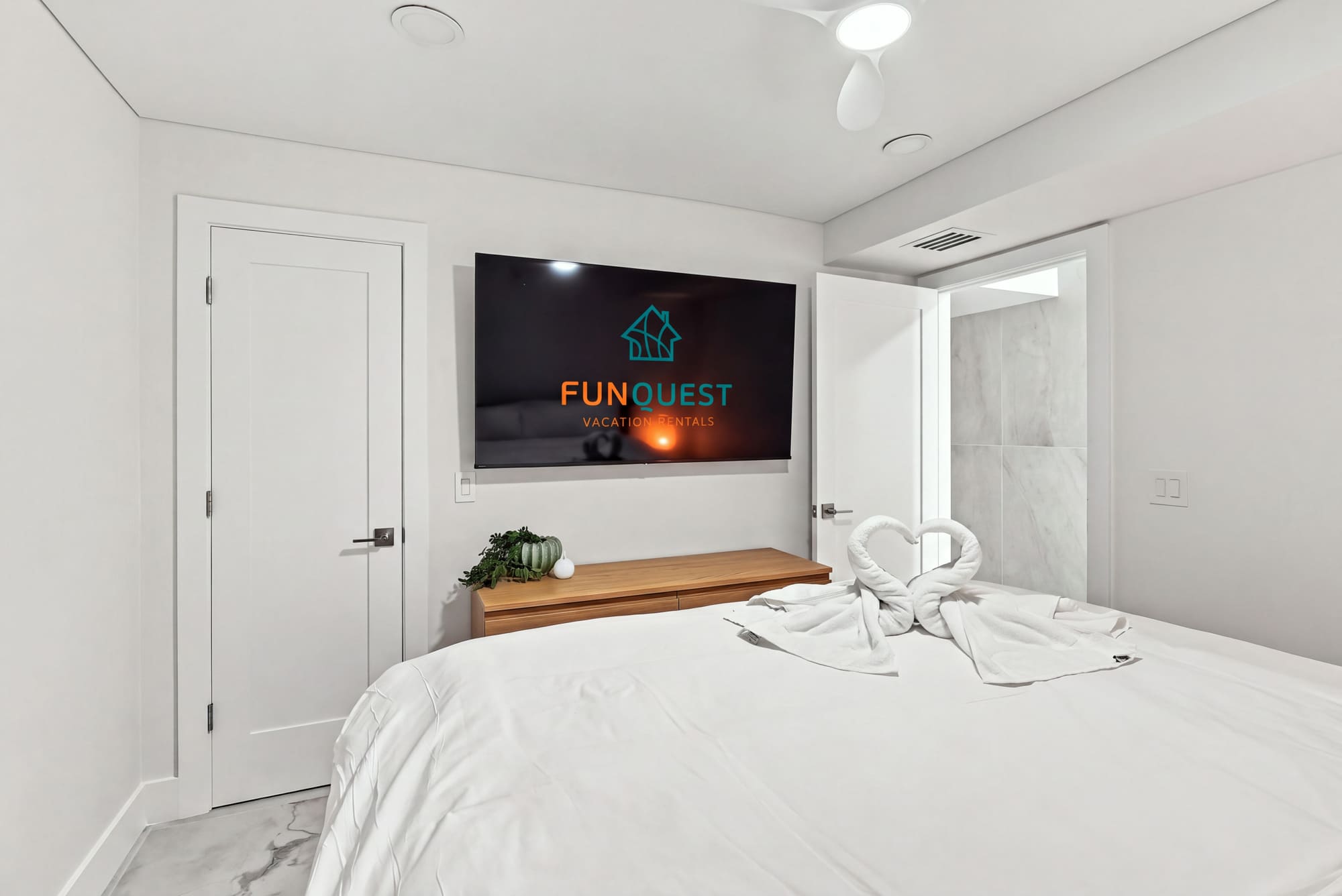 The Summit 1512 – Modern bedroom with a large TV, wooden dresser, and towel swans on the bed.