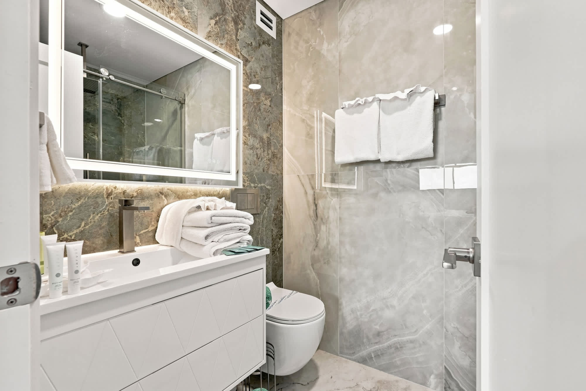 The Summit 1512 – Modern bathroom with a large mirror, glass shower, and neatly arranged towels.
