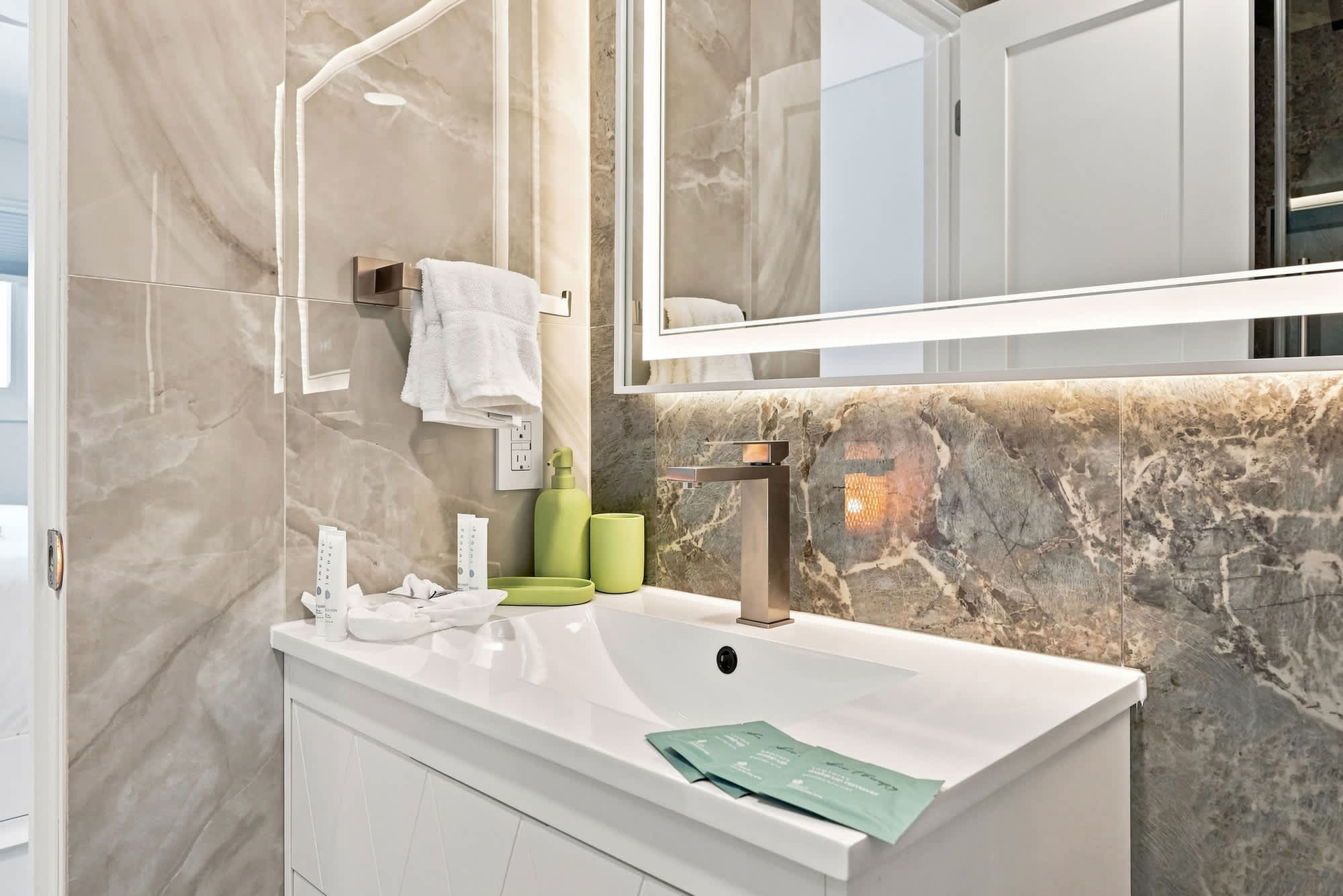 The Summit 1512 – Modern bathroom with a marble accent wall, sleek sink, and decorative green accessories.