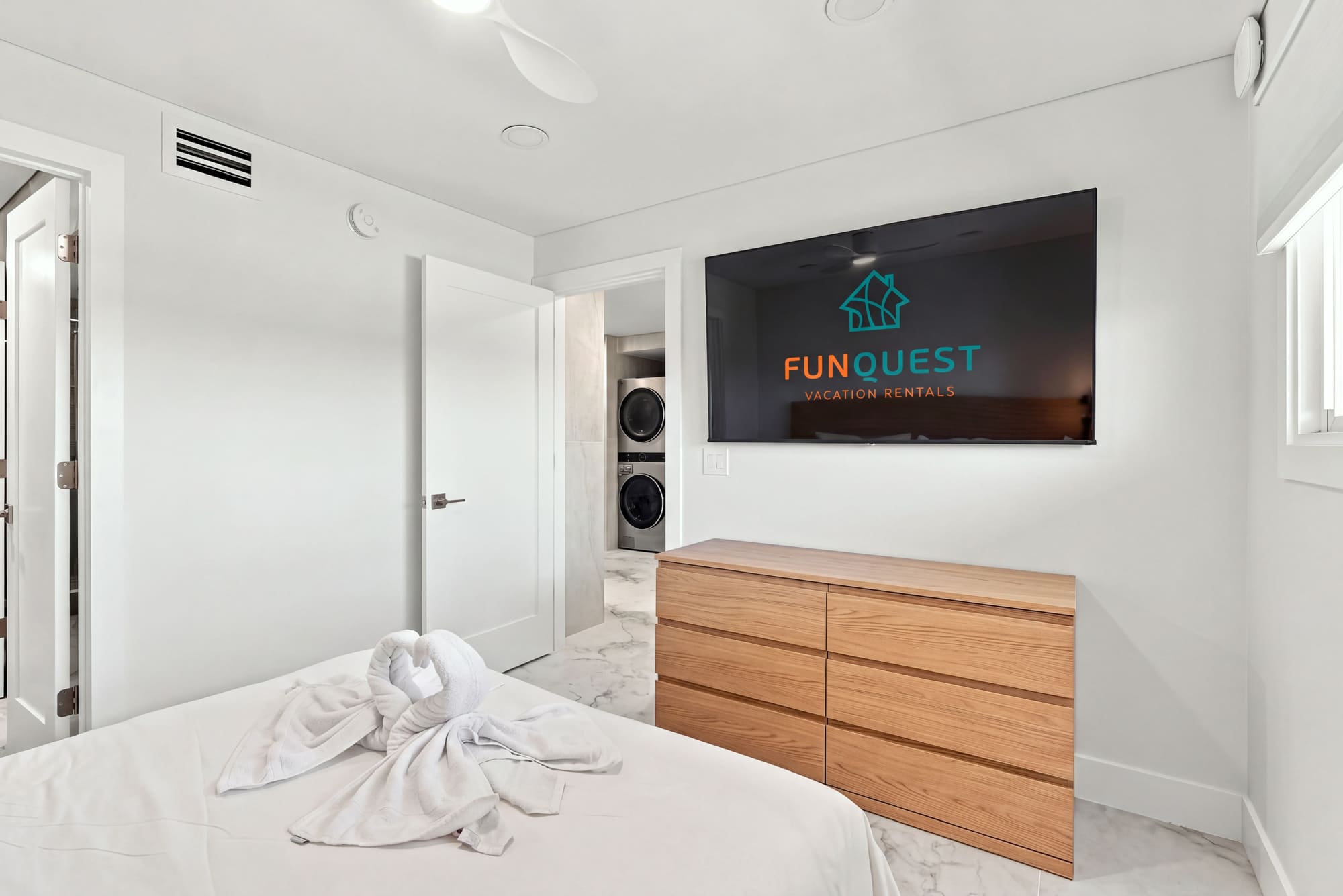 The Summit 1512 – Bedroom with a wall-mounted TV, wooden dresser, and towel swans on the bed.