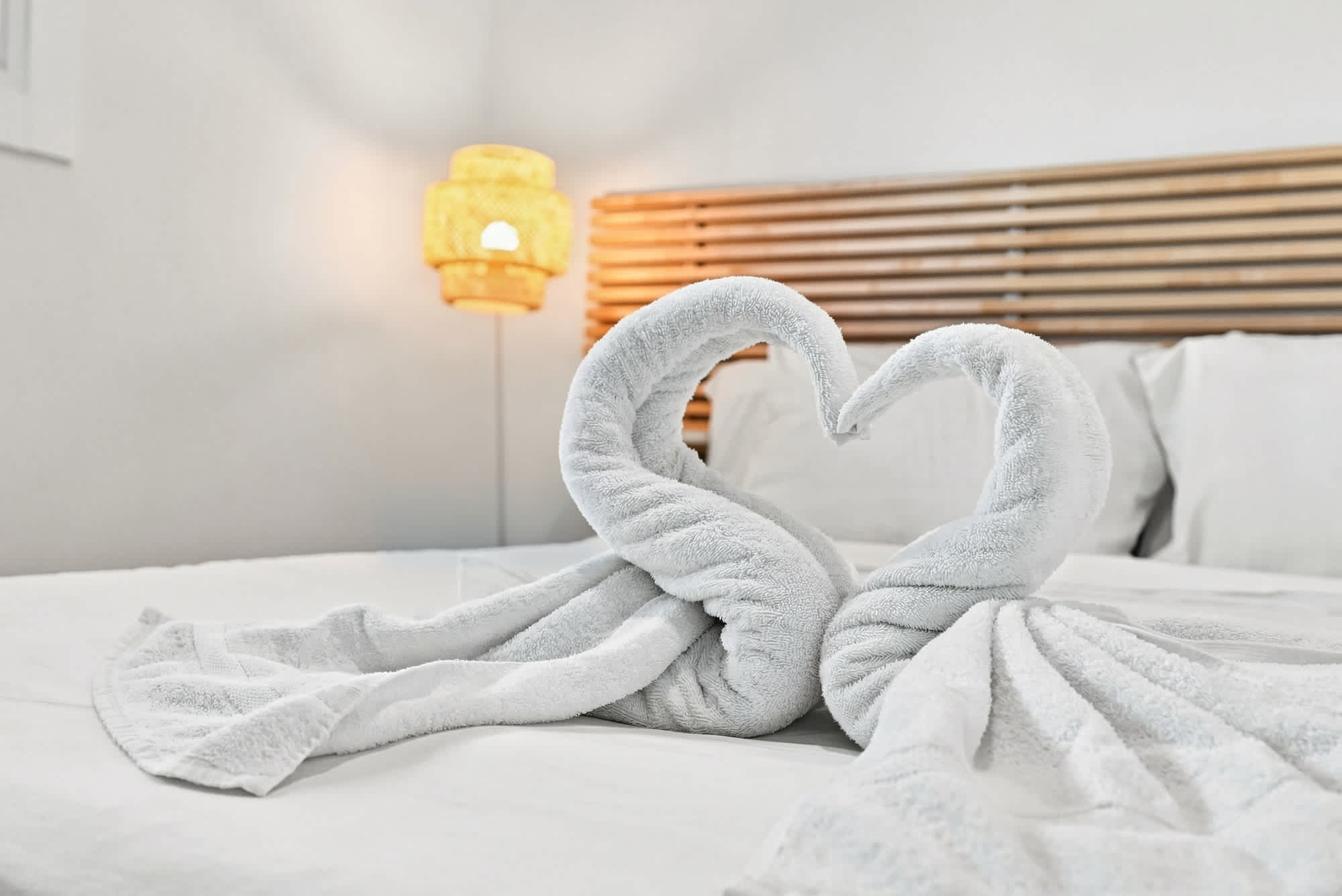 The Summit 1512 – Towel swans forming a heart shape on a neatly made bed with a wooden headboard.