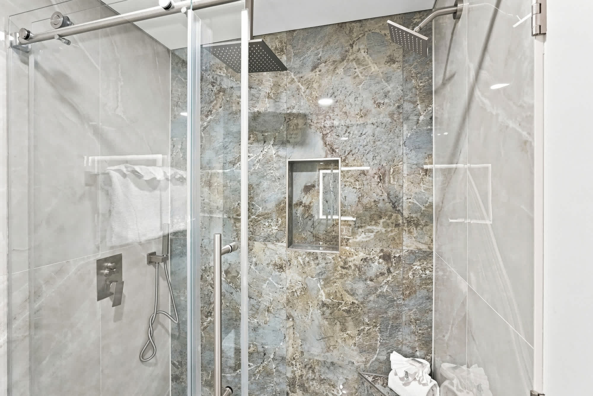 The Summit 1512 – Modern glass shower with two showerheads and marble tiles.