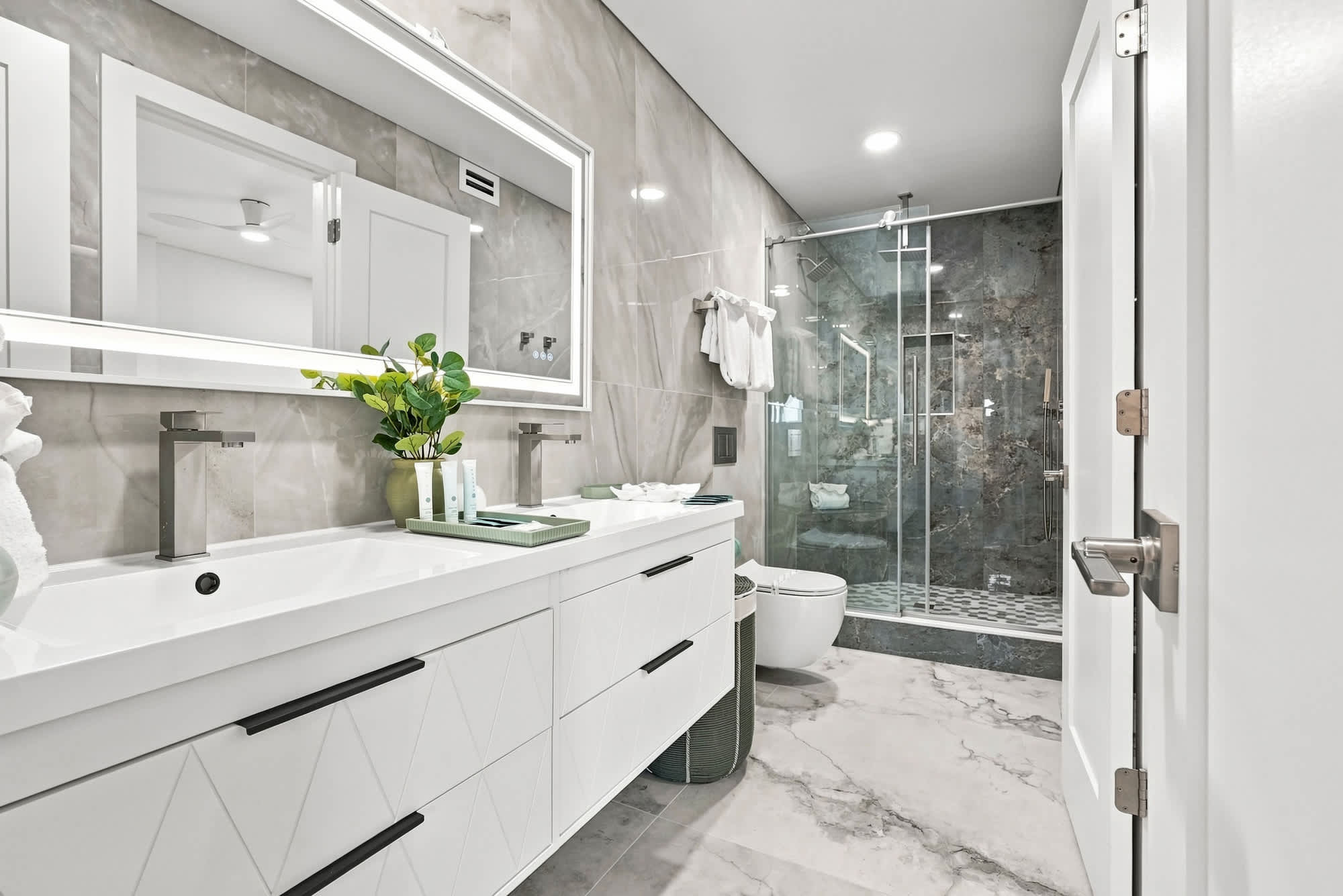 The Summit 1512 – Modern bathroom with double vanity, glass shower, and decorative plants.