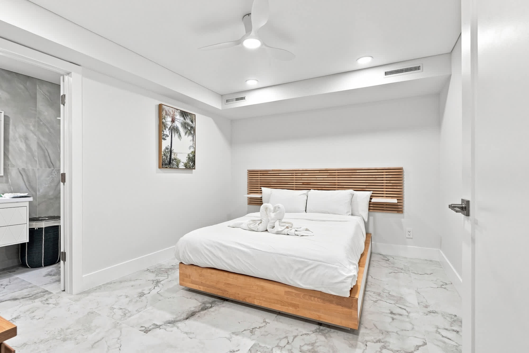 The Summit 1512 – Modern bedroom with a queen bed, marble flooring, wall art, and an ensuite bathroom doorway.