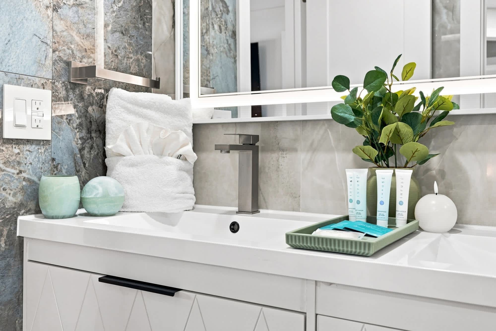 The Summit 1512 – Modern bathroom with marble walls, a sleek sink, towels, toiletries, and a decorative plant.