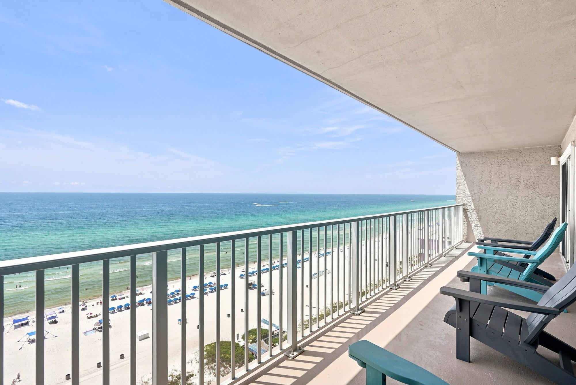 The Summit 1512 – Balcony view from The Summit 1512 overlooking beach, turquoise water, and chairs for seating.