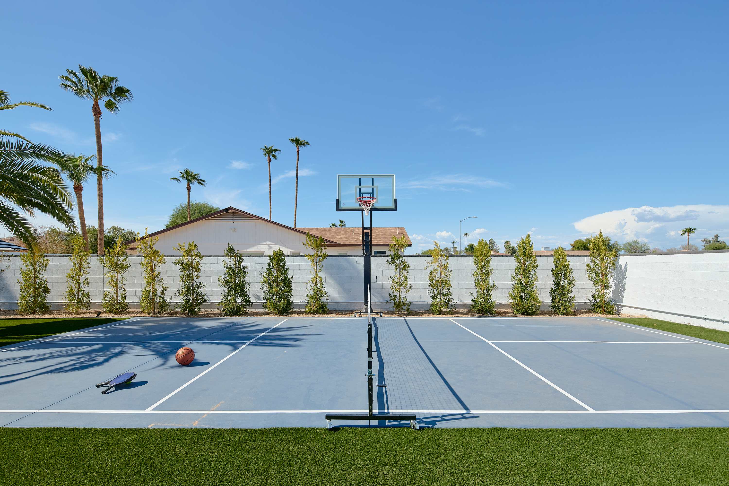 Private multi-sport court for basketball, pickleball, and tennis beside a spacious turf lawn with cornhole for even more outdoor fun.