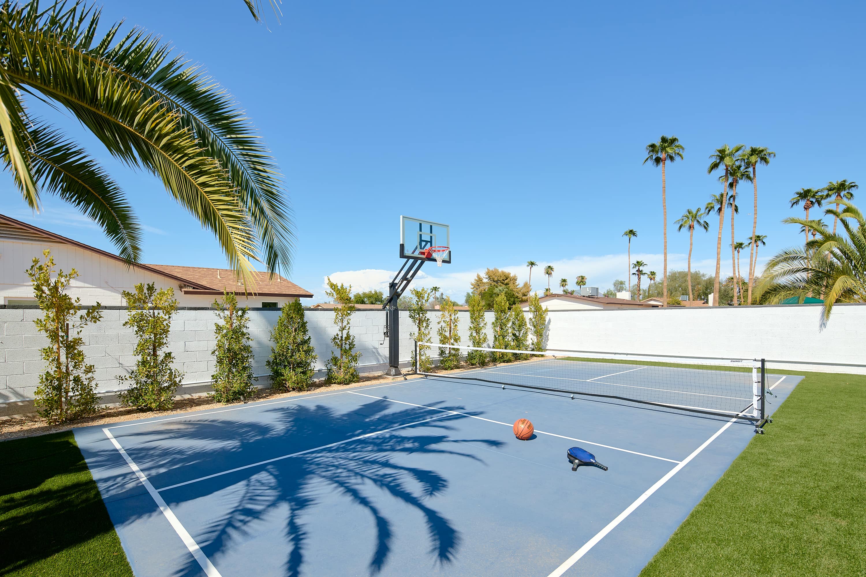 Private multi-sport court for basketball, pickleball, and tennis beside a spacious turf lawn with cornhole for even more outdoor fun.