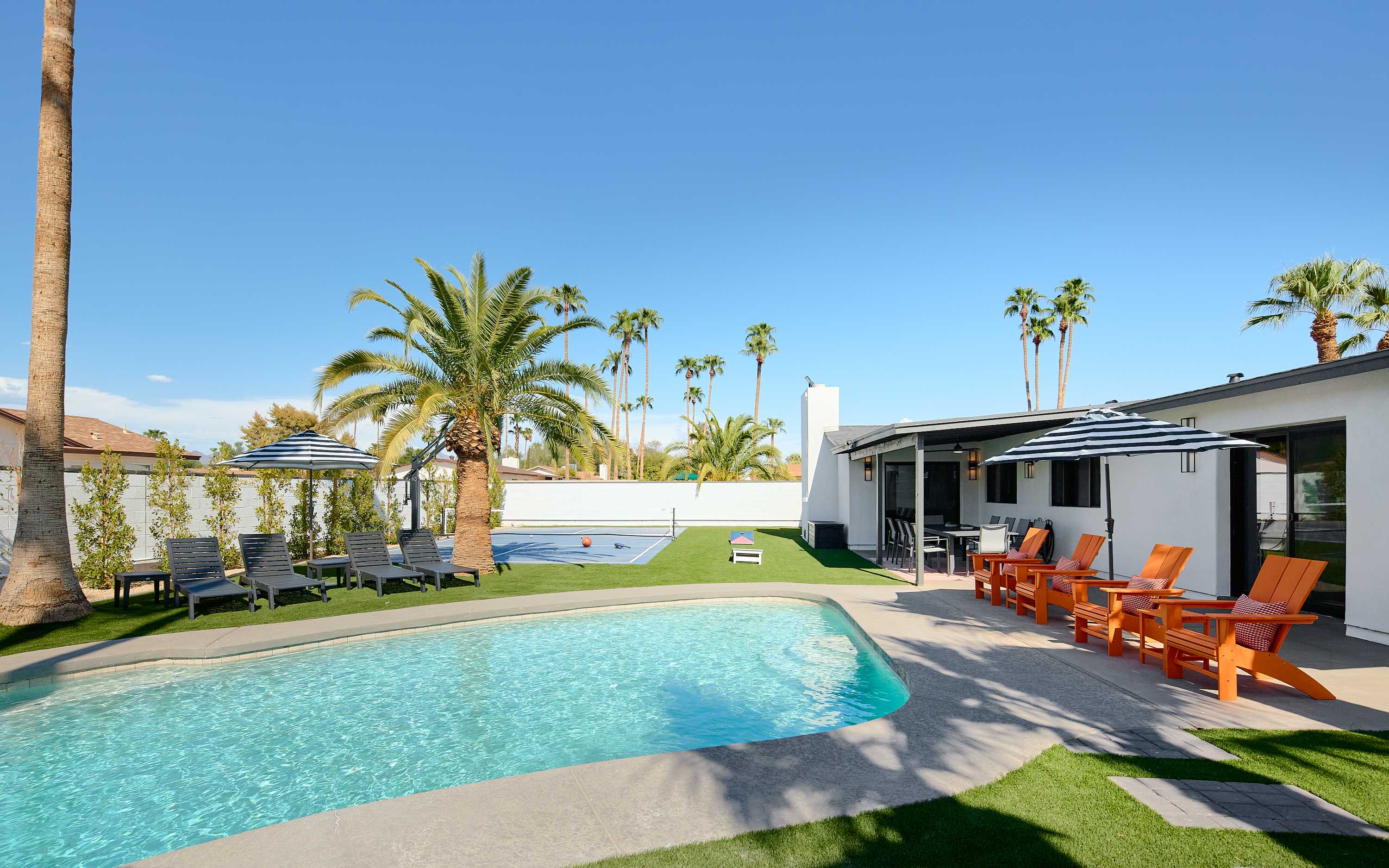 Resort-style backyard featuring a private pool, poolside loungers, a multi-sport court for basketball, pickleball, and tennis, turf with cornhole, a pergola with a built-in BBQ and bar seating, and a covered patio with outdoor dining table for 10.